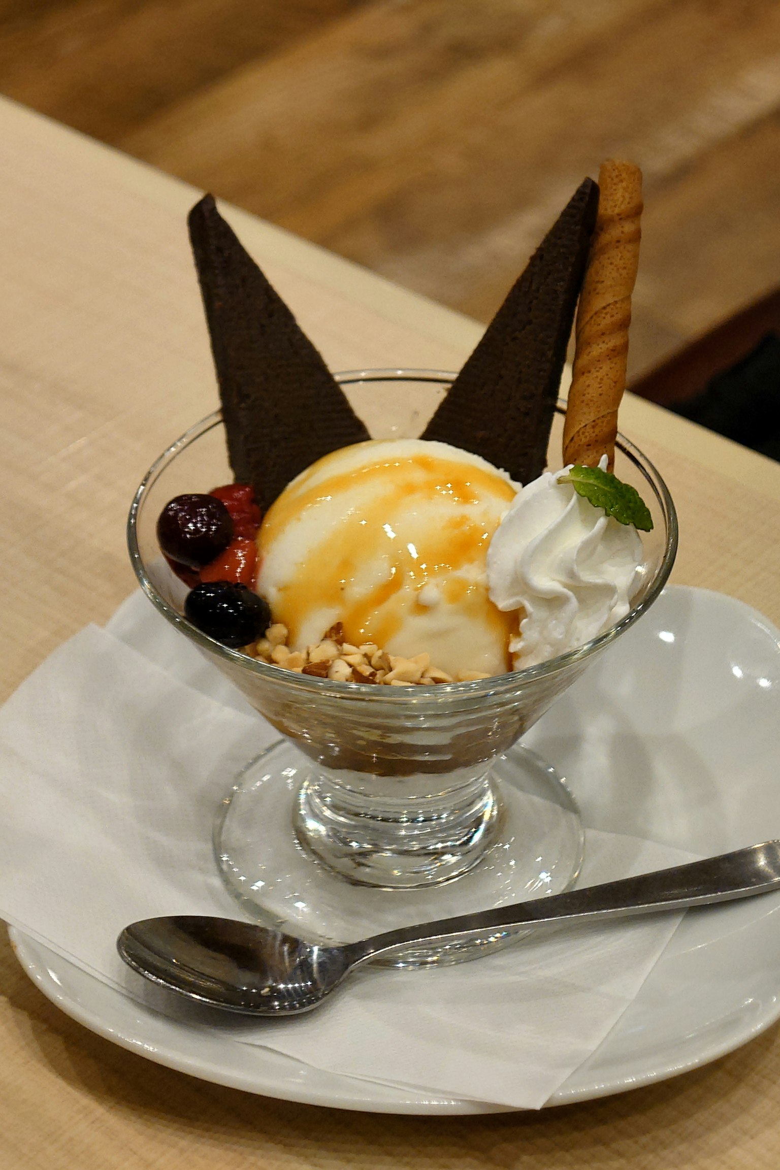 Dessert cup with ice cream topped with chocolate triangles and a cookie alongside fruits