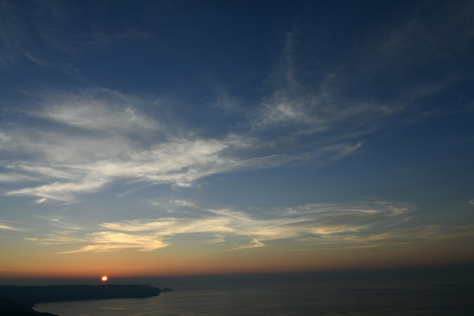 Matahari terbenam di laut dengan langit biru dan awan
