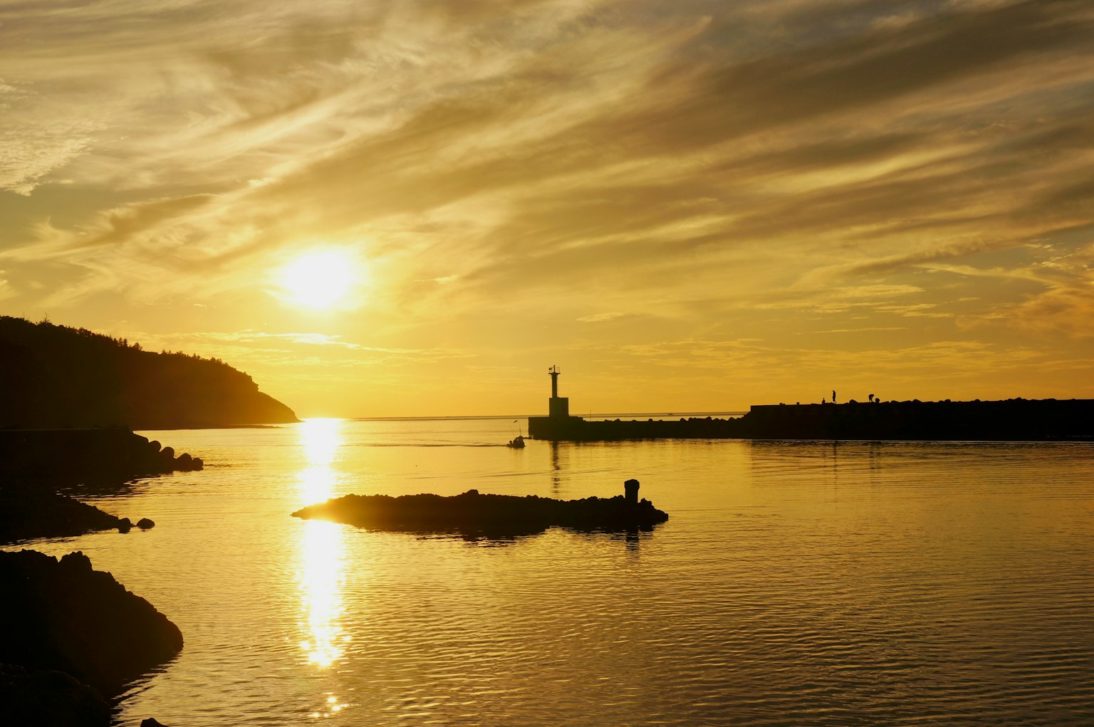 Scène de coucher de soleil côtier avec un phare réfléchissant sur des eaux calmes