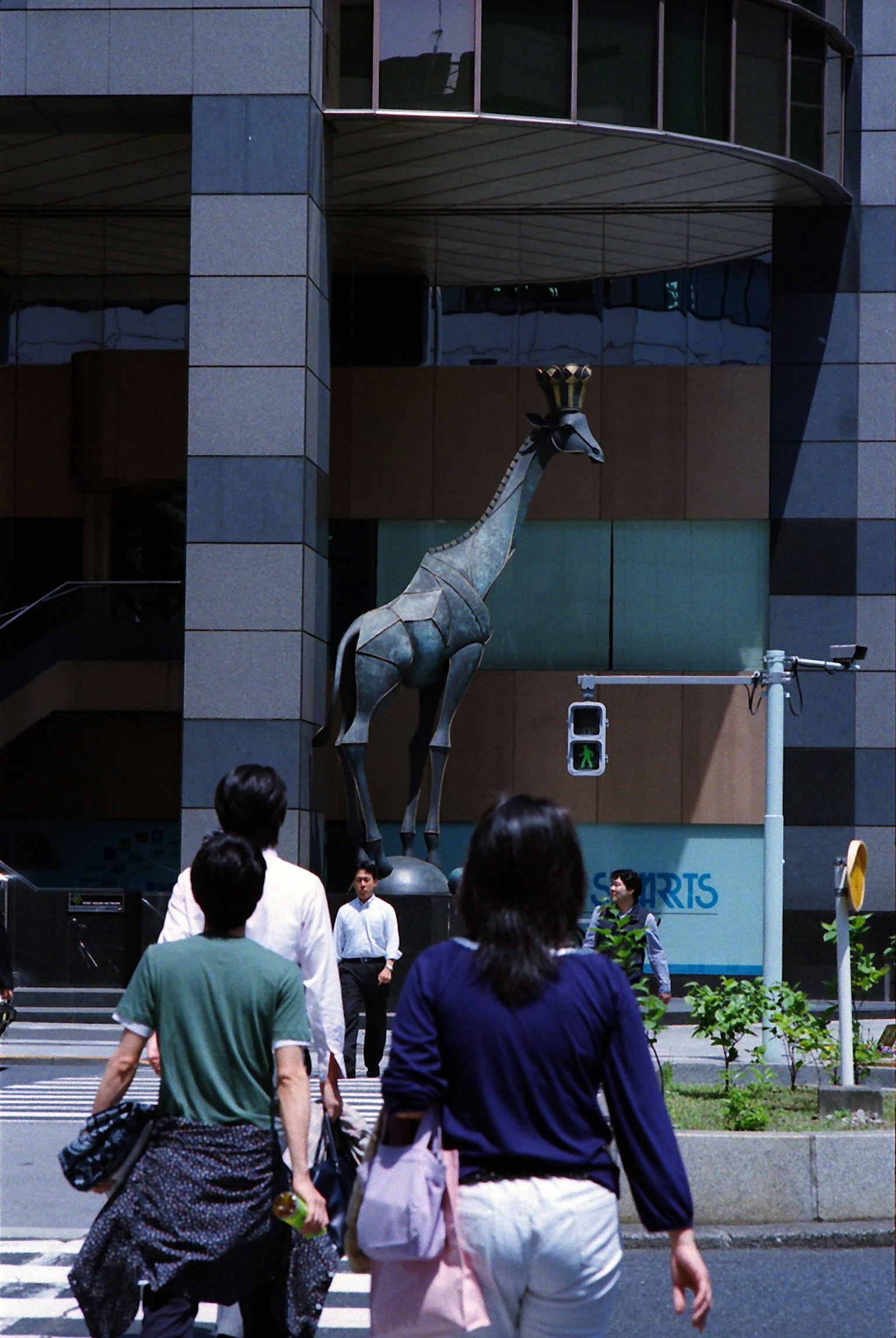 Persone che camminano per strada con una scultura di giraffa coronata in vista