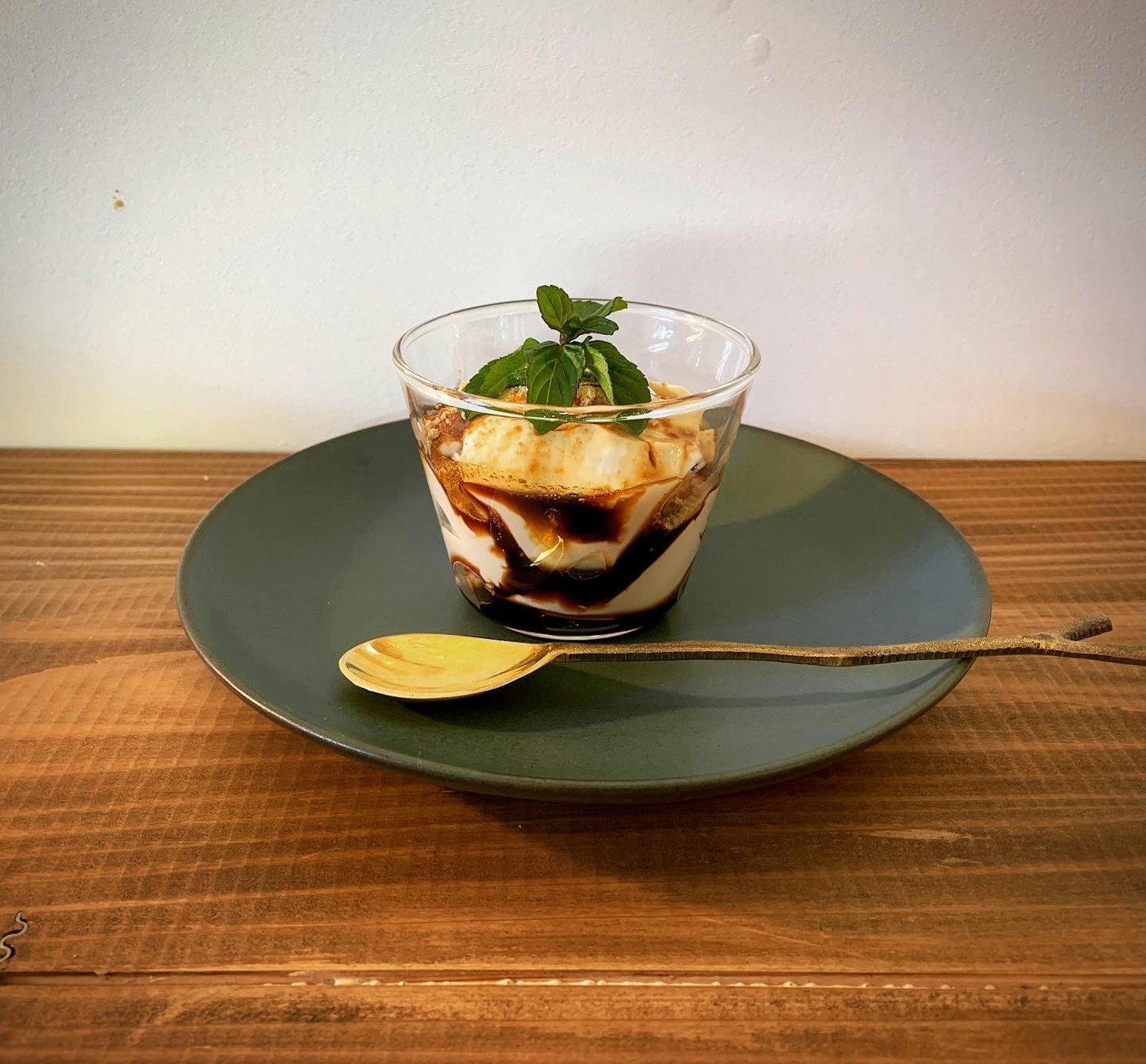 Dessertglas auf einem grünen Teller mit Schichten aus Banane und Sahne garniert mit einem Minzblatt