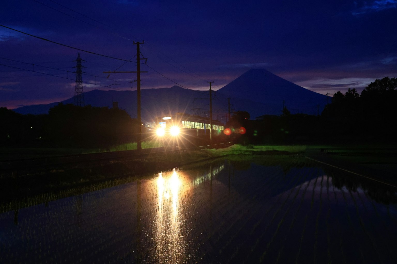 火車燈光照亮黃昏時的山脈和稻田