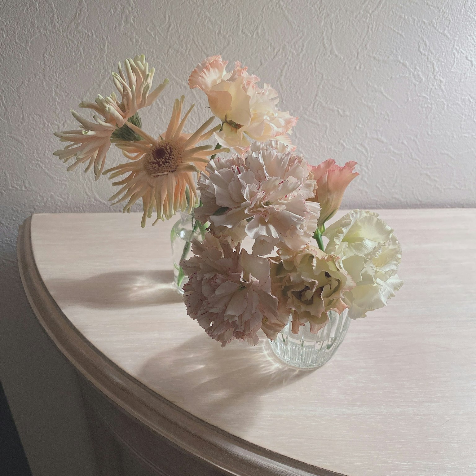 A glass vase filled with soft-colored flowers placed on a table