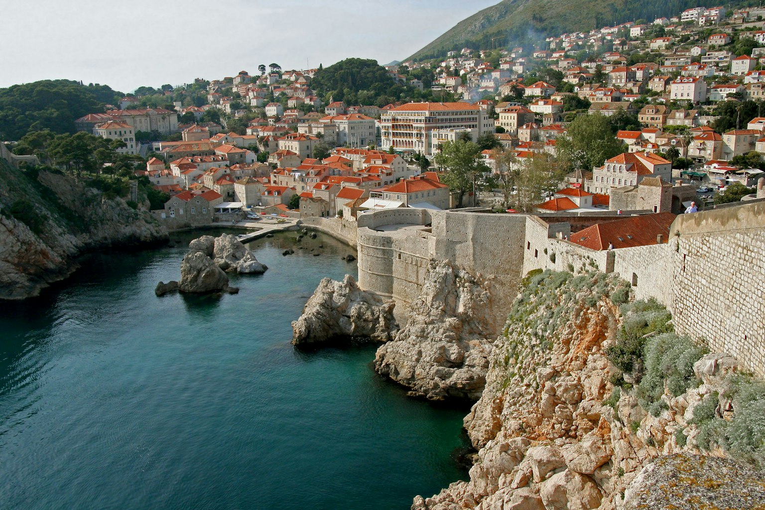 Ancient city walls along a serene sea with orange-roofed houses