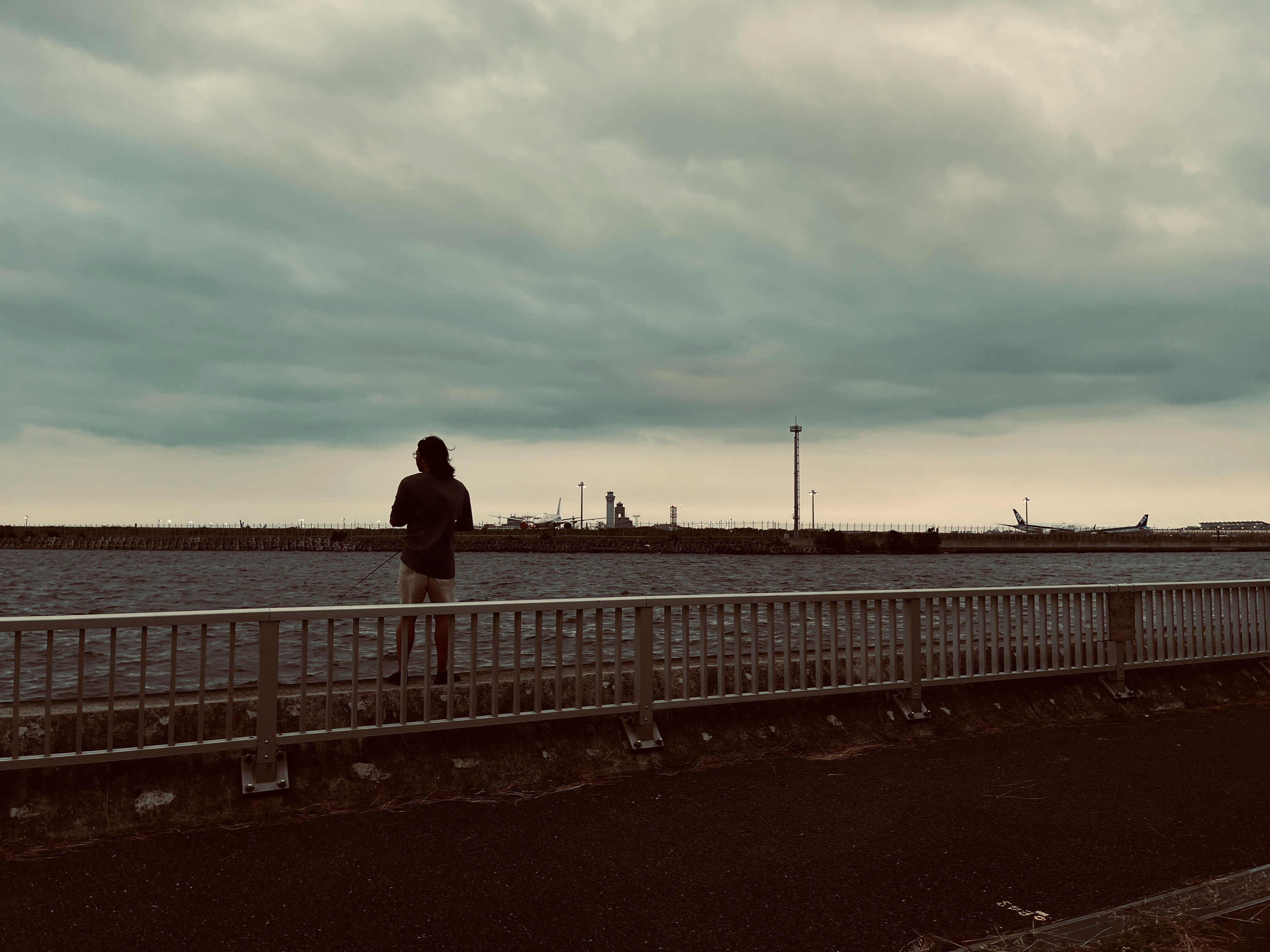 Person fishing on a seaside pier under an overcast sky