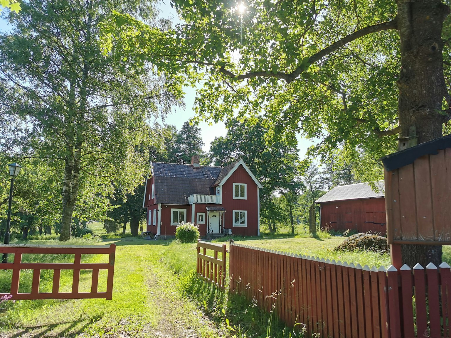 Scenic view of a red house surrounded by lush greenery and a wooden fence