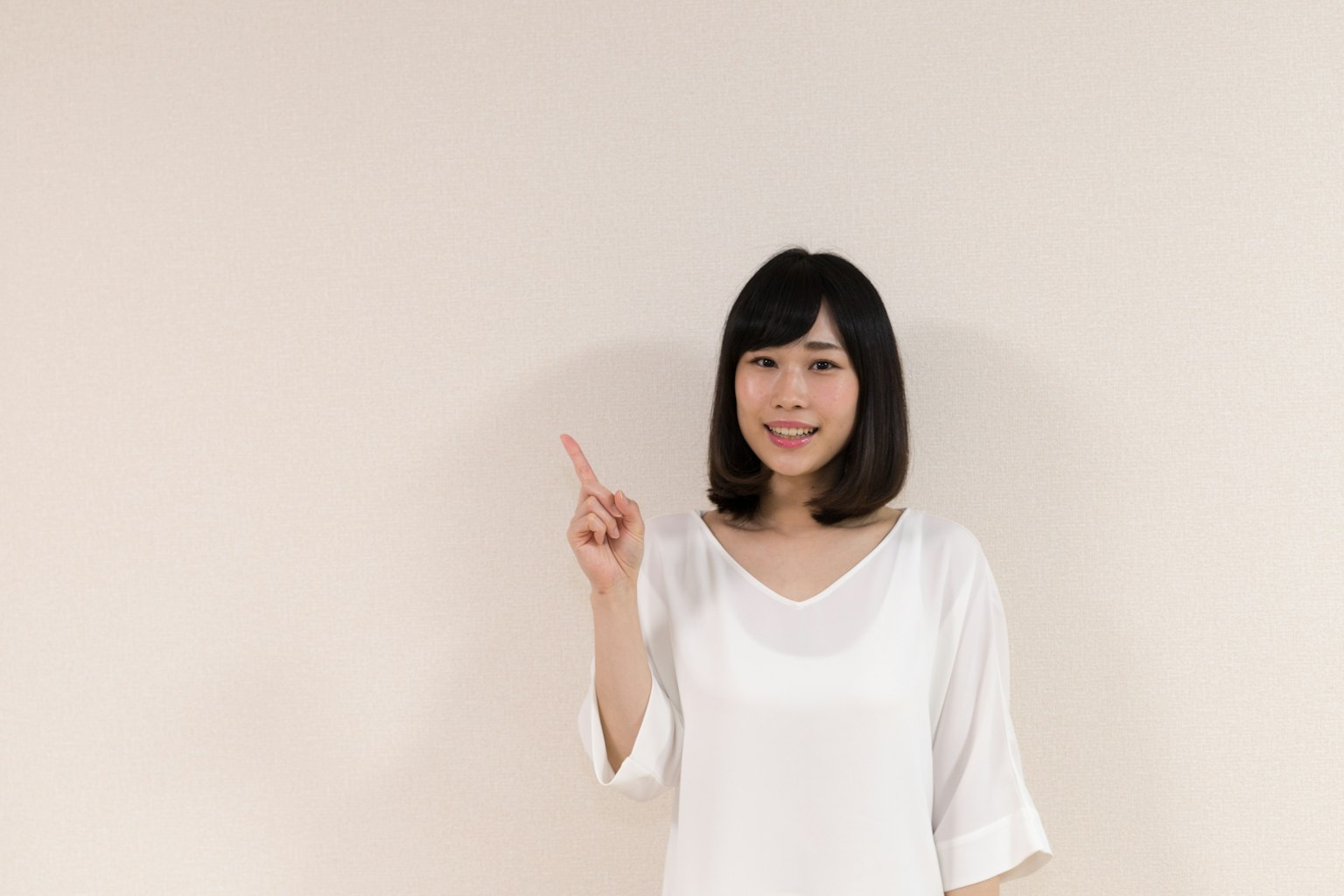 A woman in a white shirt smiling and pointing upwards