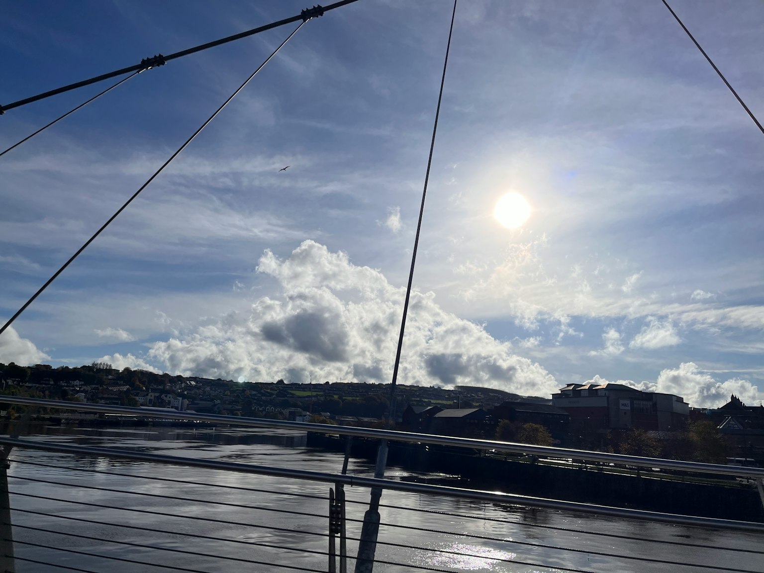藍天和雲彩的河邊景色 橋樑纜索可見 太陽在照耀