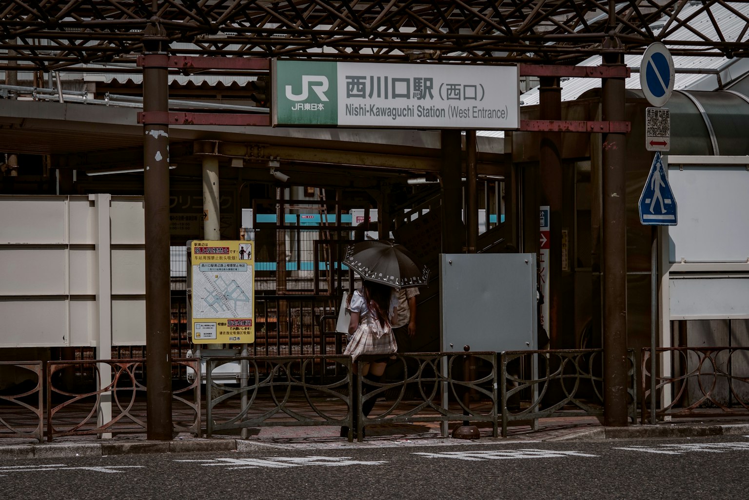 Eingang der Nishikawaguchi Station mit einer Person, die einen Regenschirm hält