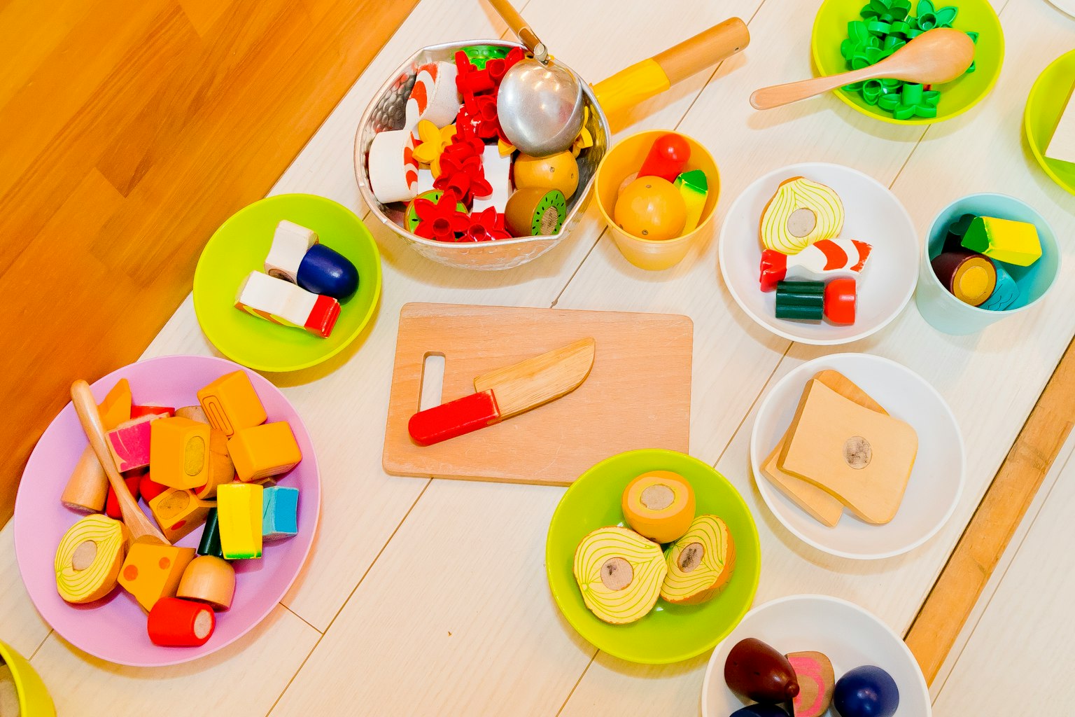 Colorful toy food items arranged in bowls and plates in a play area