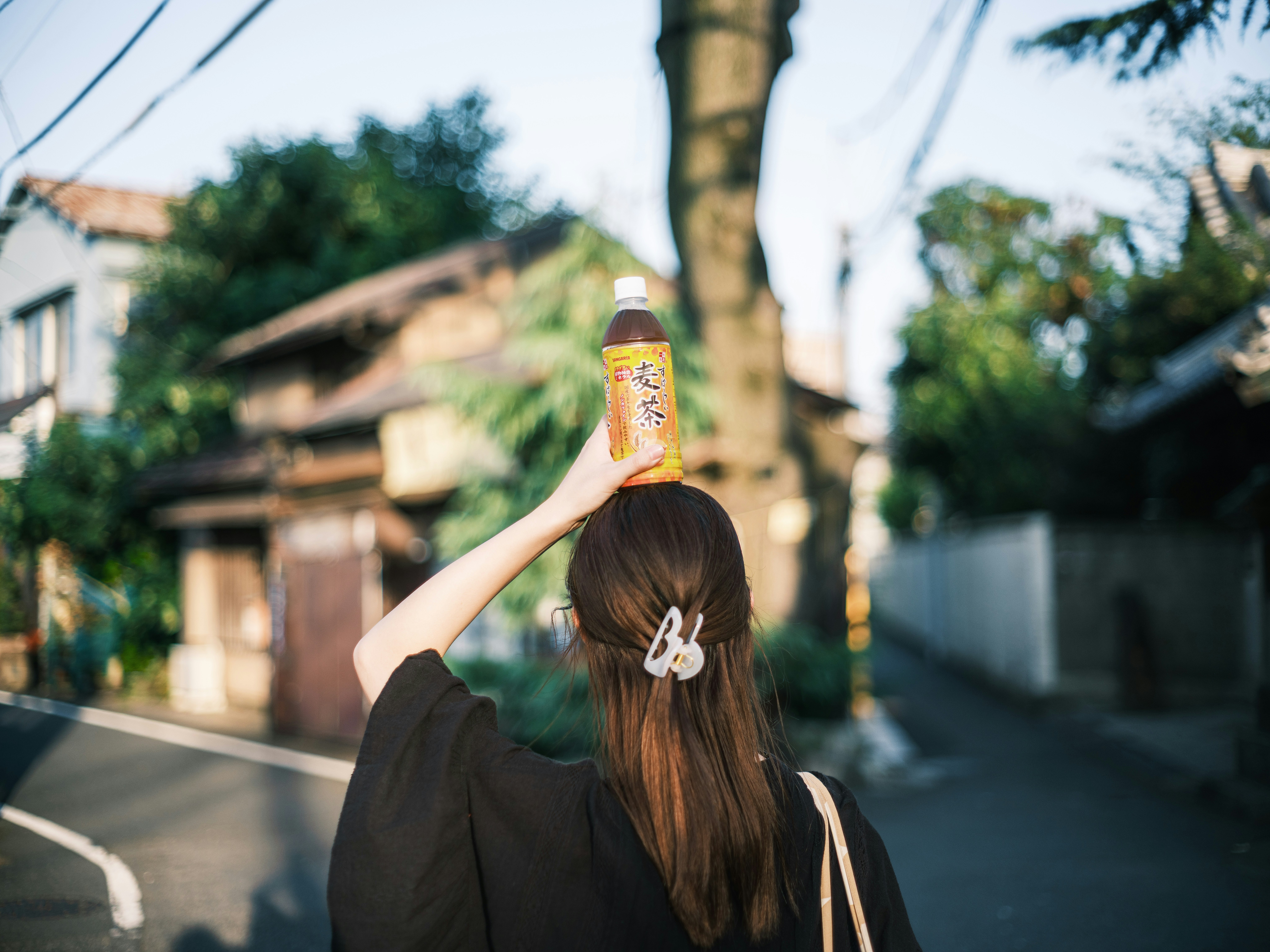 路地を歩く女性が飲み物の缶を頭上に掲げる