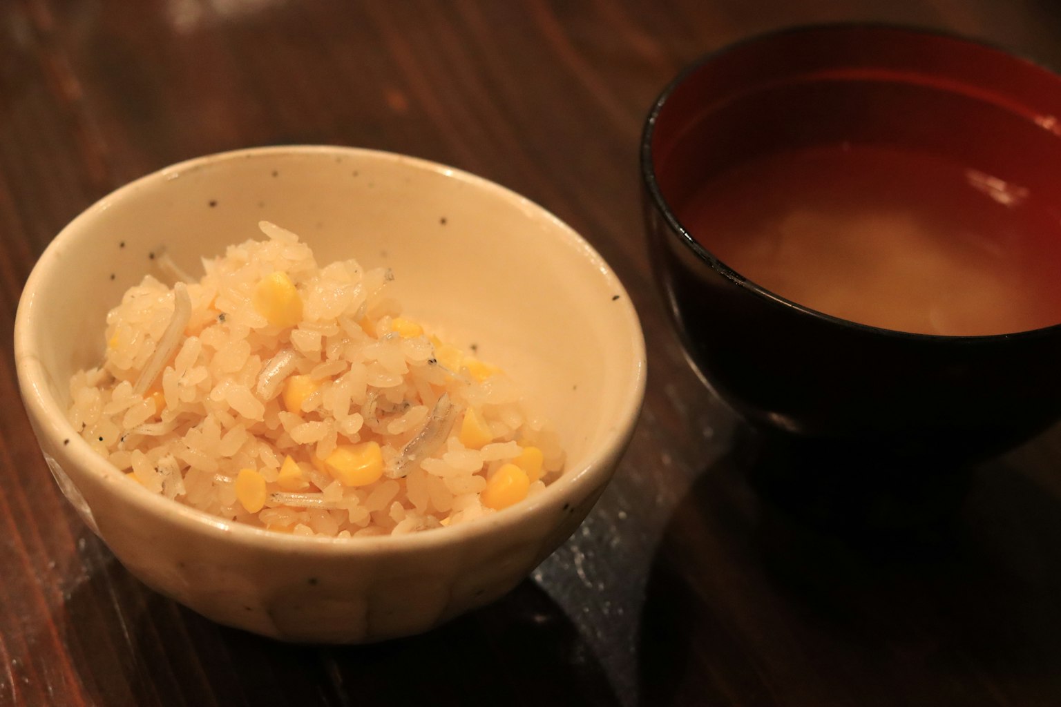 Mangkuk nasi dengan jagung dan semangkuk sup miso di atas meja kayu