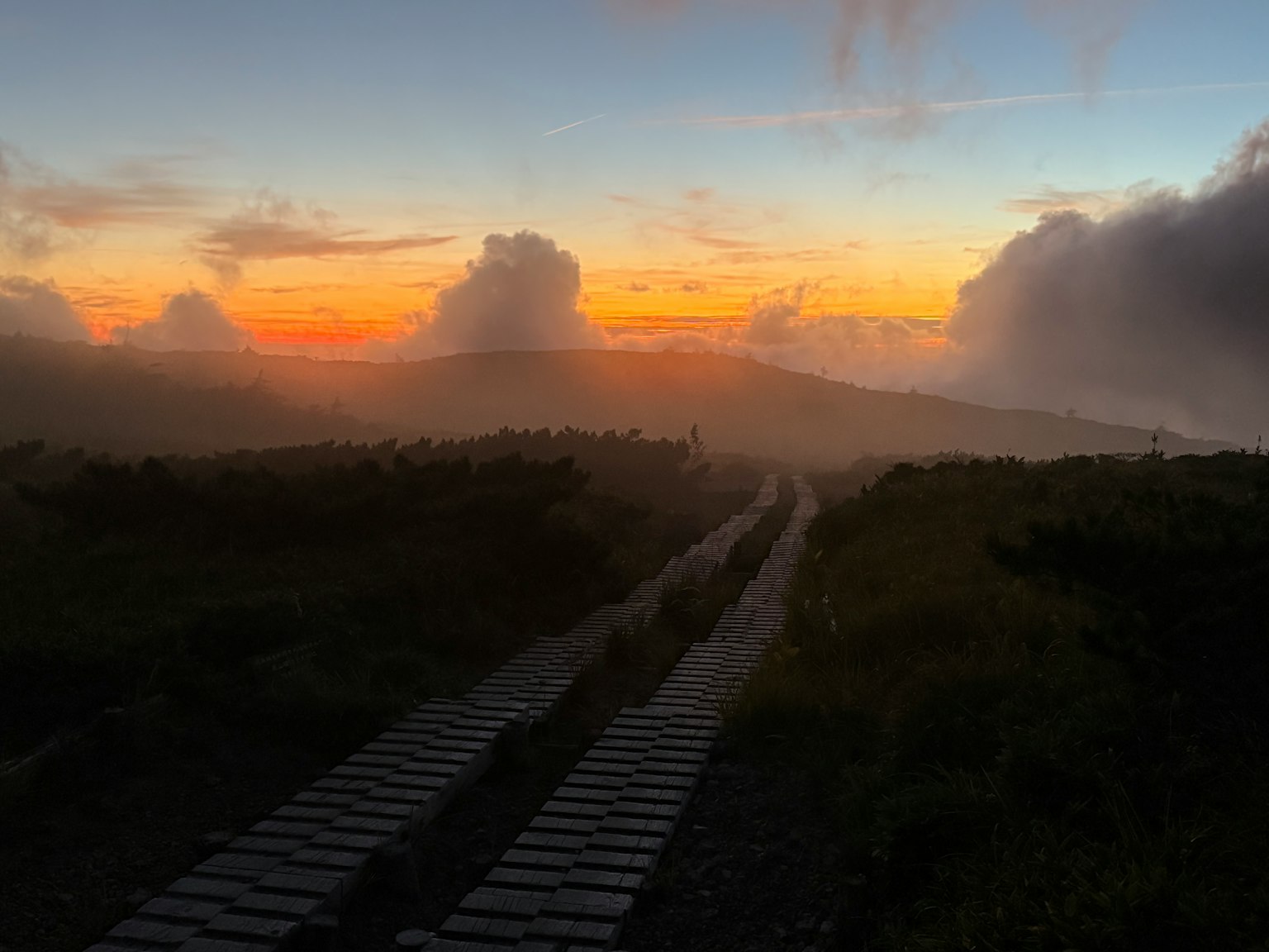 Vista escénica del atardecer con nubes y niebla camino de madera que lleva al horizonte