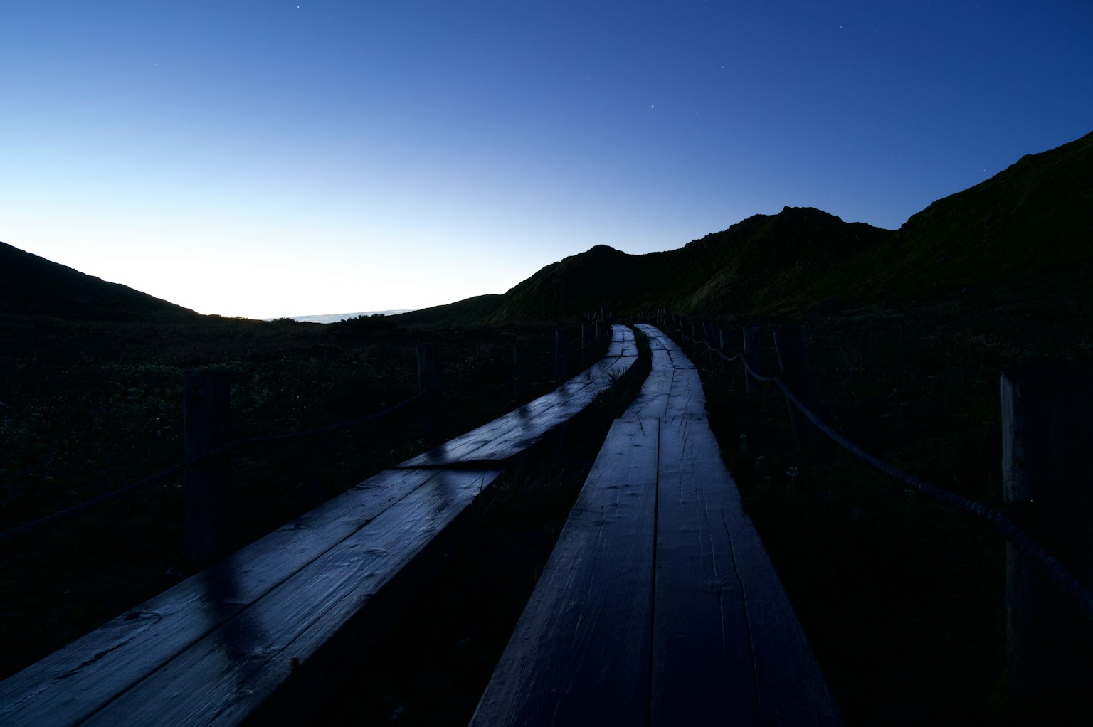 Sentier en bois menant au crépuscule avec des collines environnantes