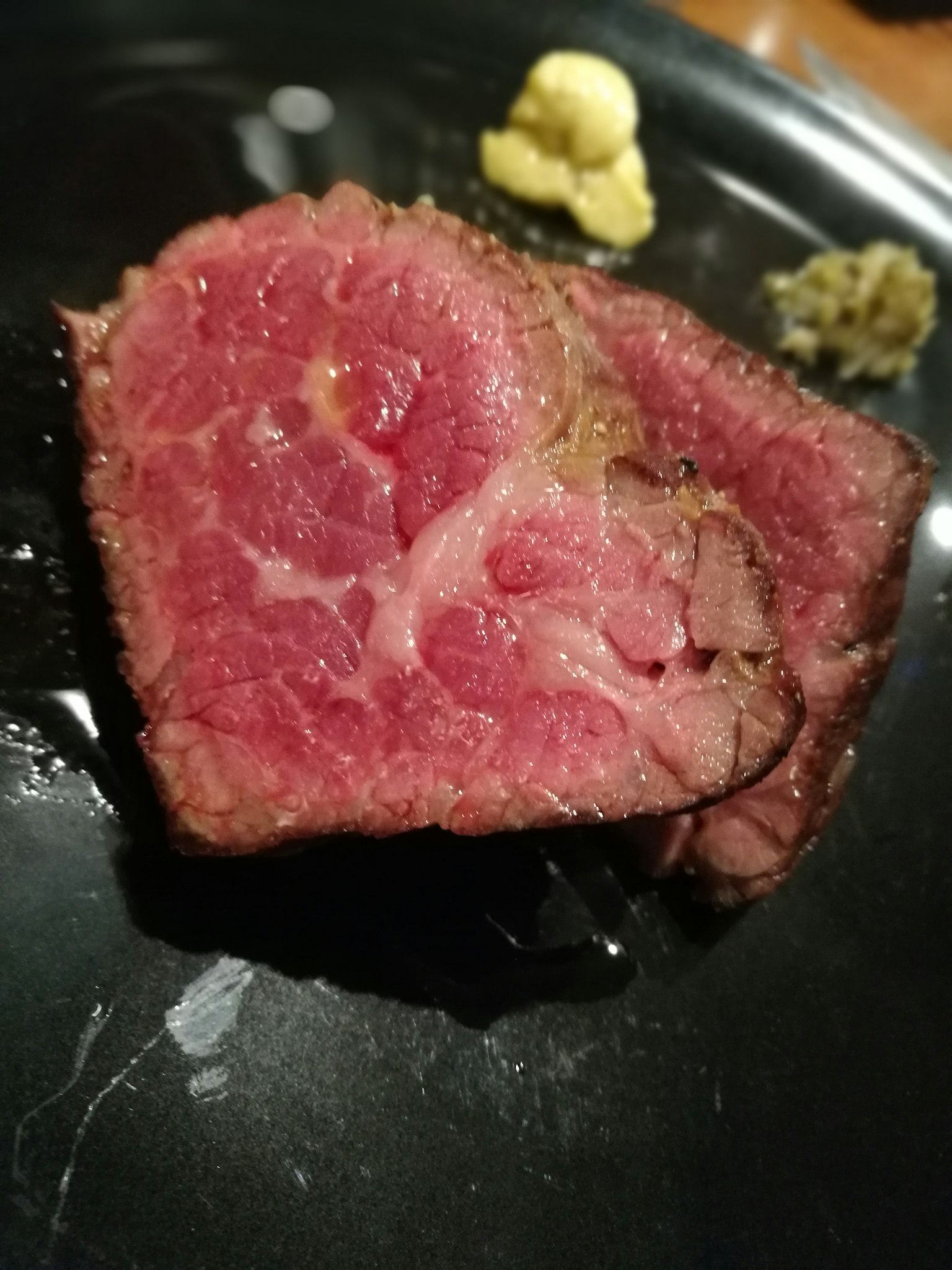 Tranche de viande rouge sur une assiette noire avec de la moutarde