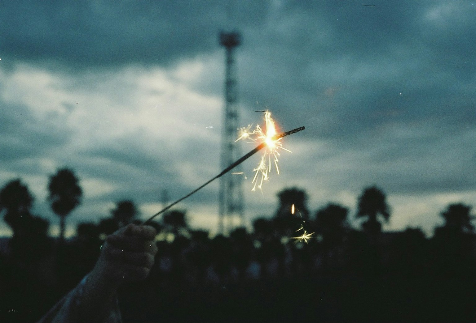 Person holding a sparkler with a dark sky background