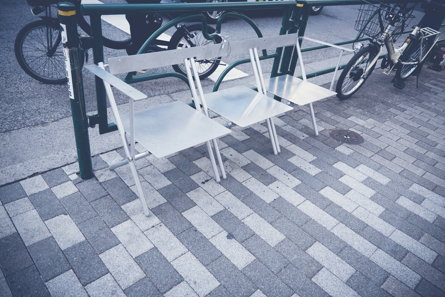Metal chairs lined up on a sidewalk with bicycles in the background