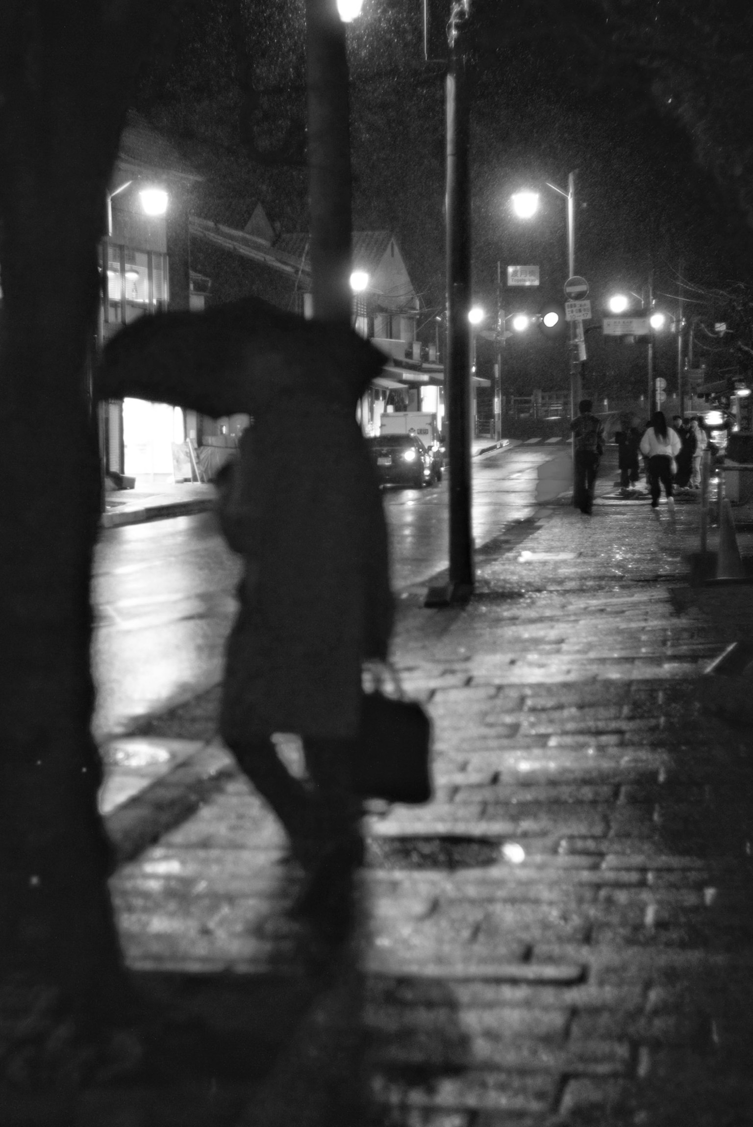 Silueta de una persona sosteniendo un paraguas en una escena de calle nocturna lluviosa