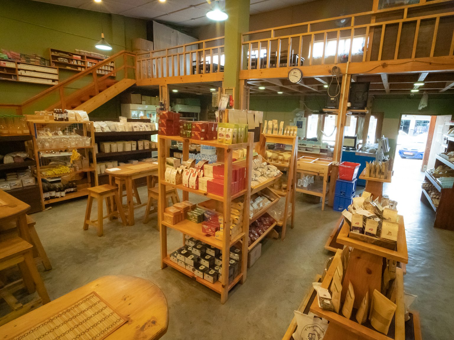 Vista interior de una tienda con estantes de madera llenos de productos iluminación brillante y paredes verdes