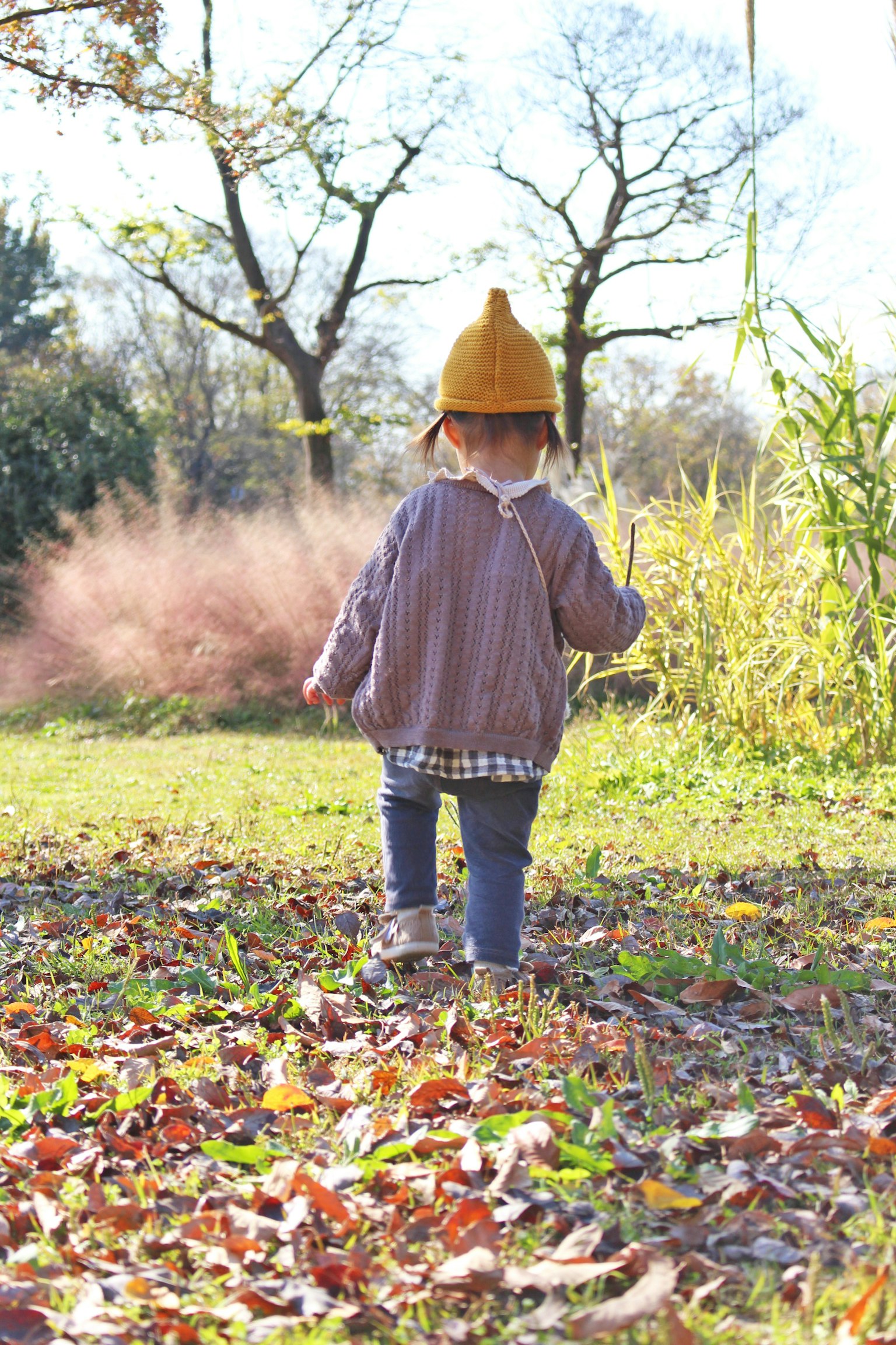 Kind, das auf Blättern in einem herbstlichen Park mit einem gelben Hut von hinten läuft