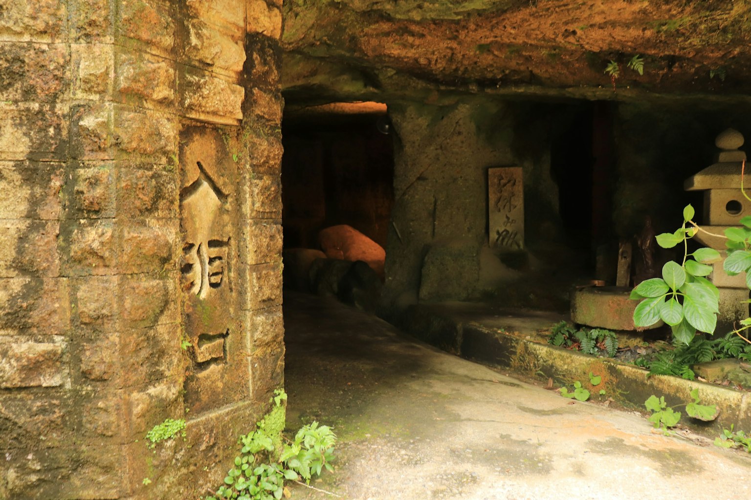 Eingang einer felsigen Höhle mit alten Inschriften und grünen Pflanzen