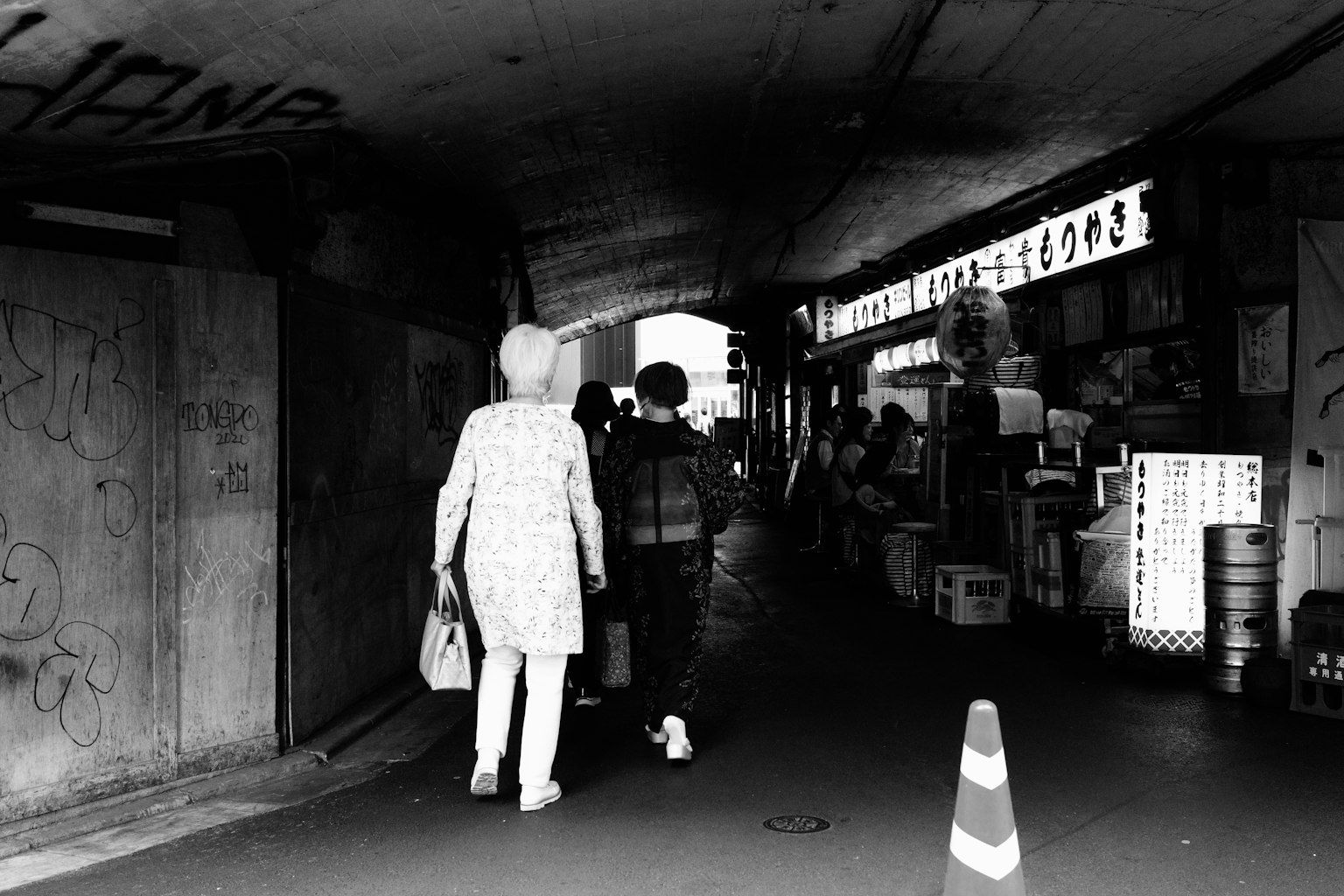 Silhouettes of two people walking under a black and white tunnel with surrounding shops