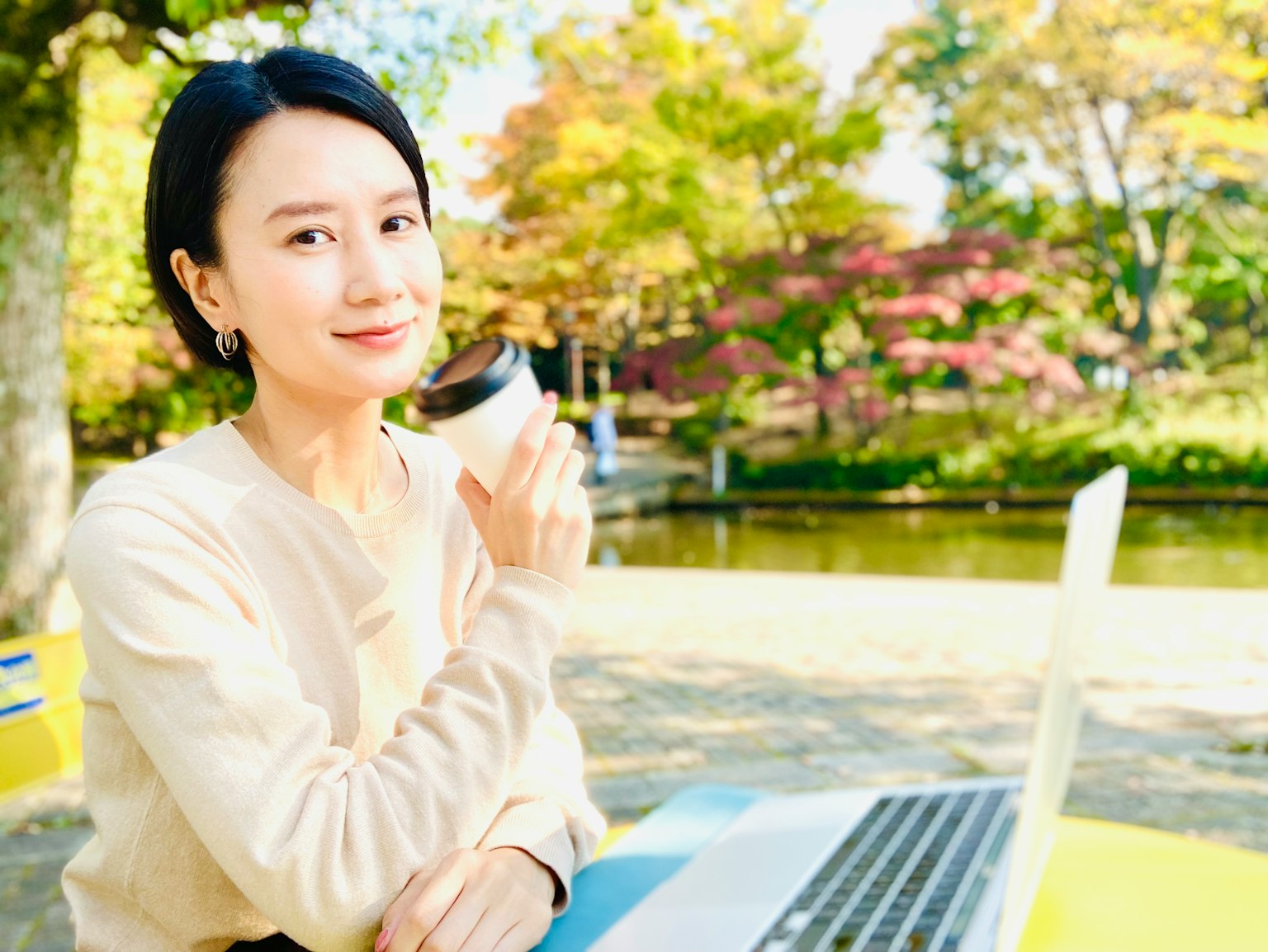 公园长椅上坐着的女性手持咖啡和笔记本电脑