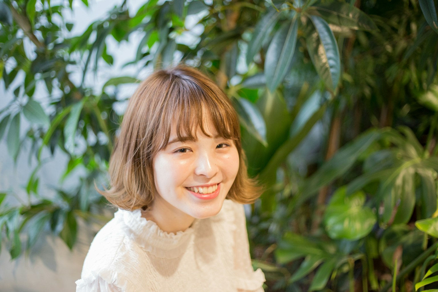 微笑的女性被綠色植物包圍,穿著休閒白色上衣