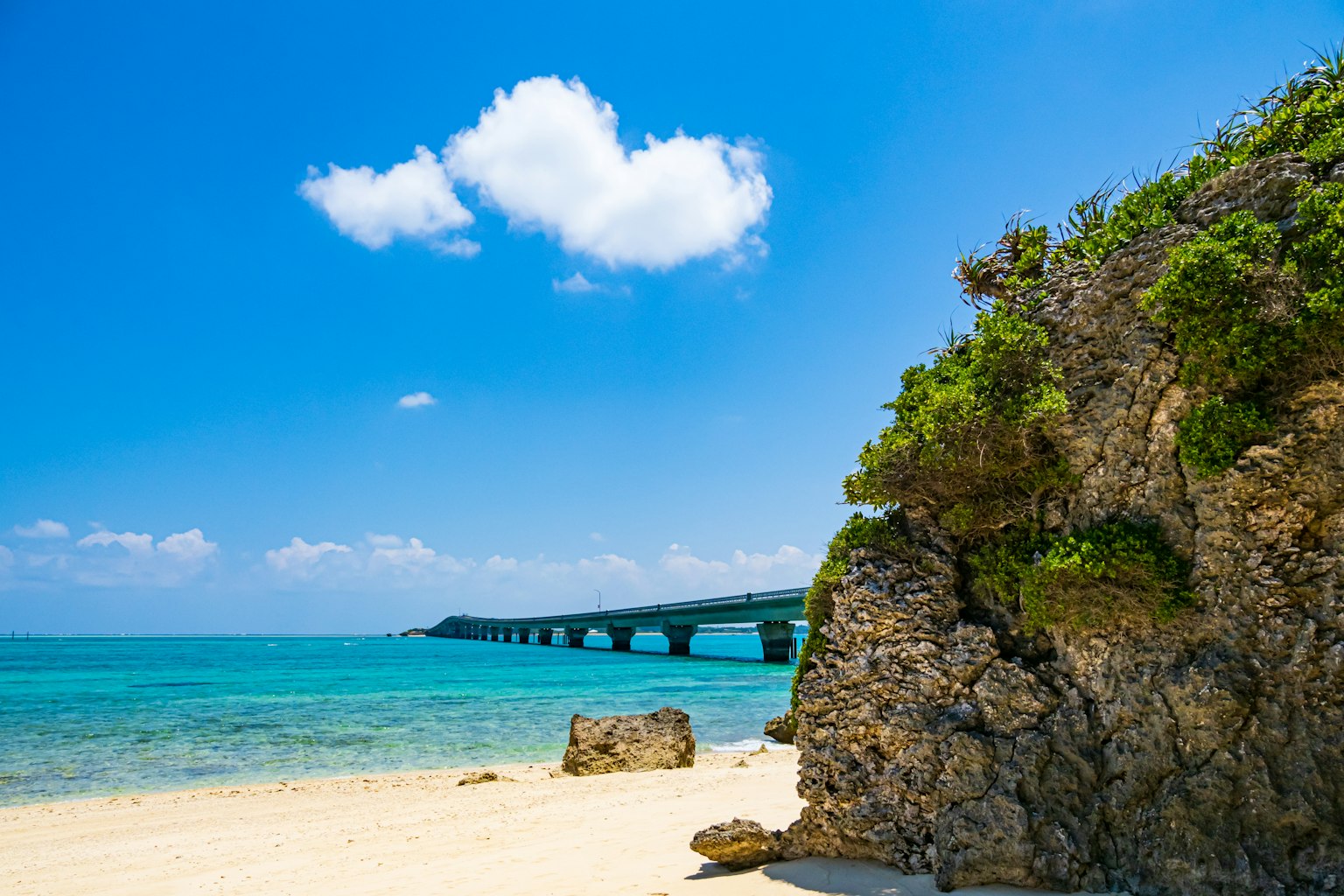 Scenic view of blue sea and sky with a bridge and rocky beach