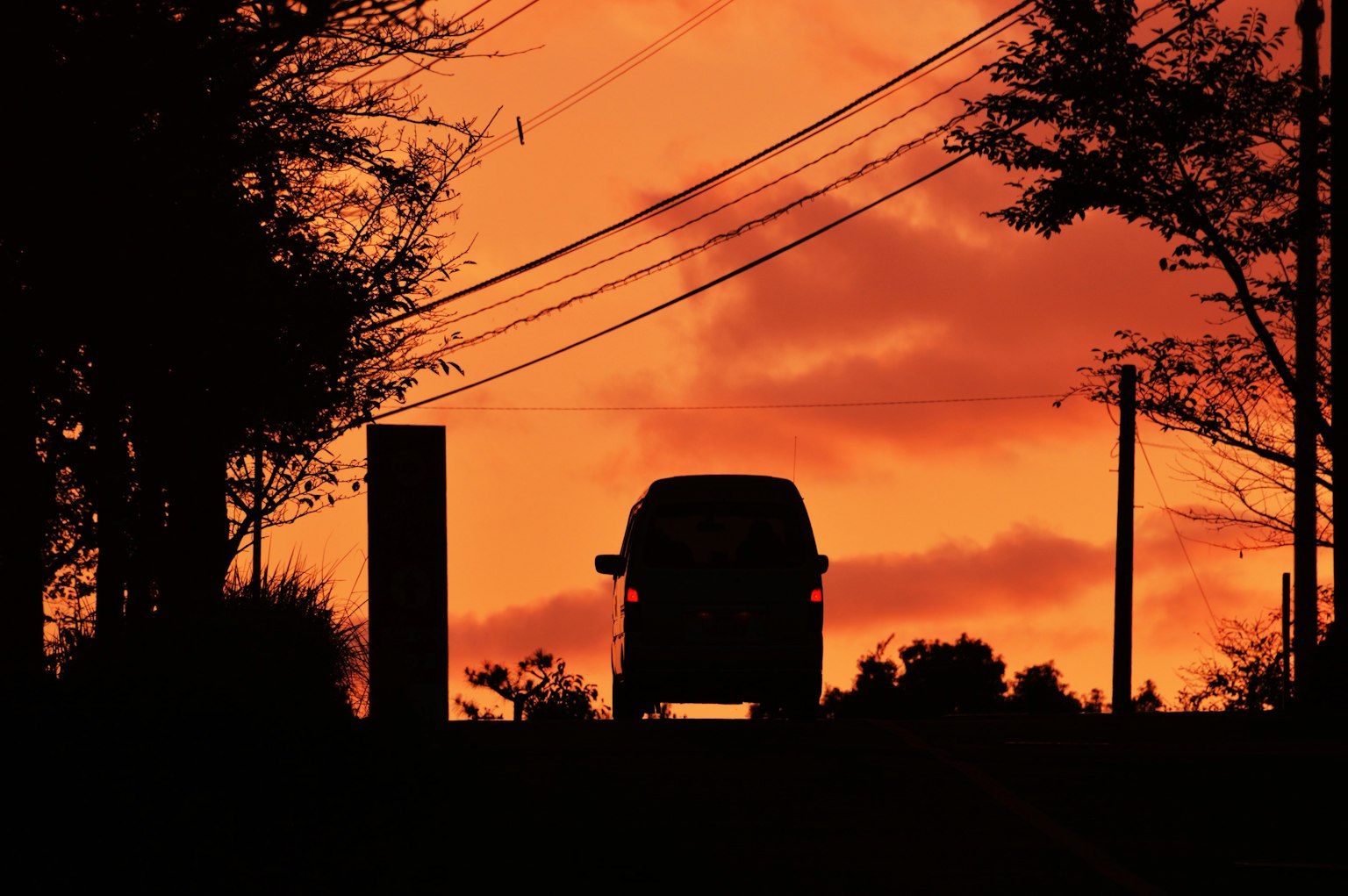 Silhouette eines Autos vor einem lebhaften Sonnenuntergang mit Bäumen