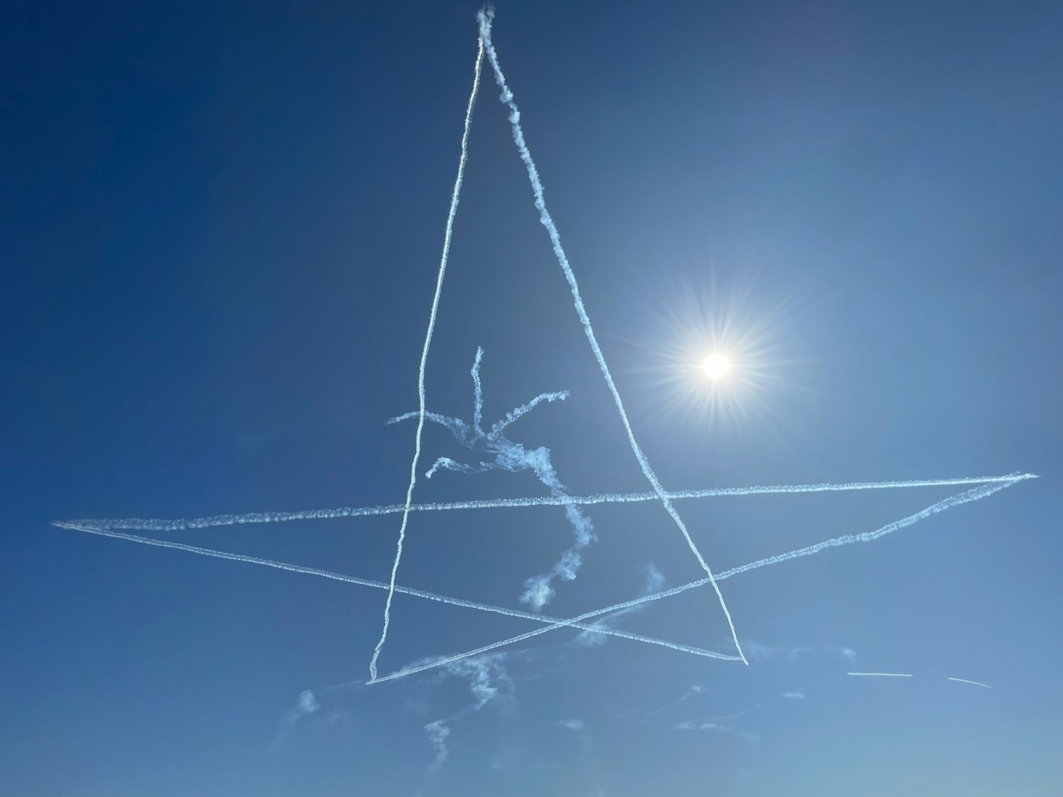 Grande scia di fumo a forma di stella nel cielo blu con il sole