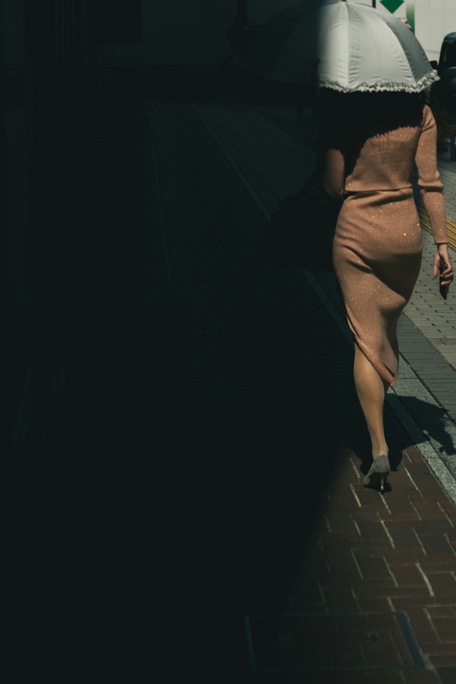 Una donna che cammina in un vestito beige con un ombrello in una strada di città