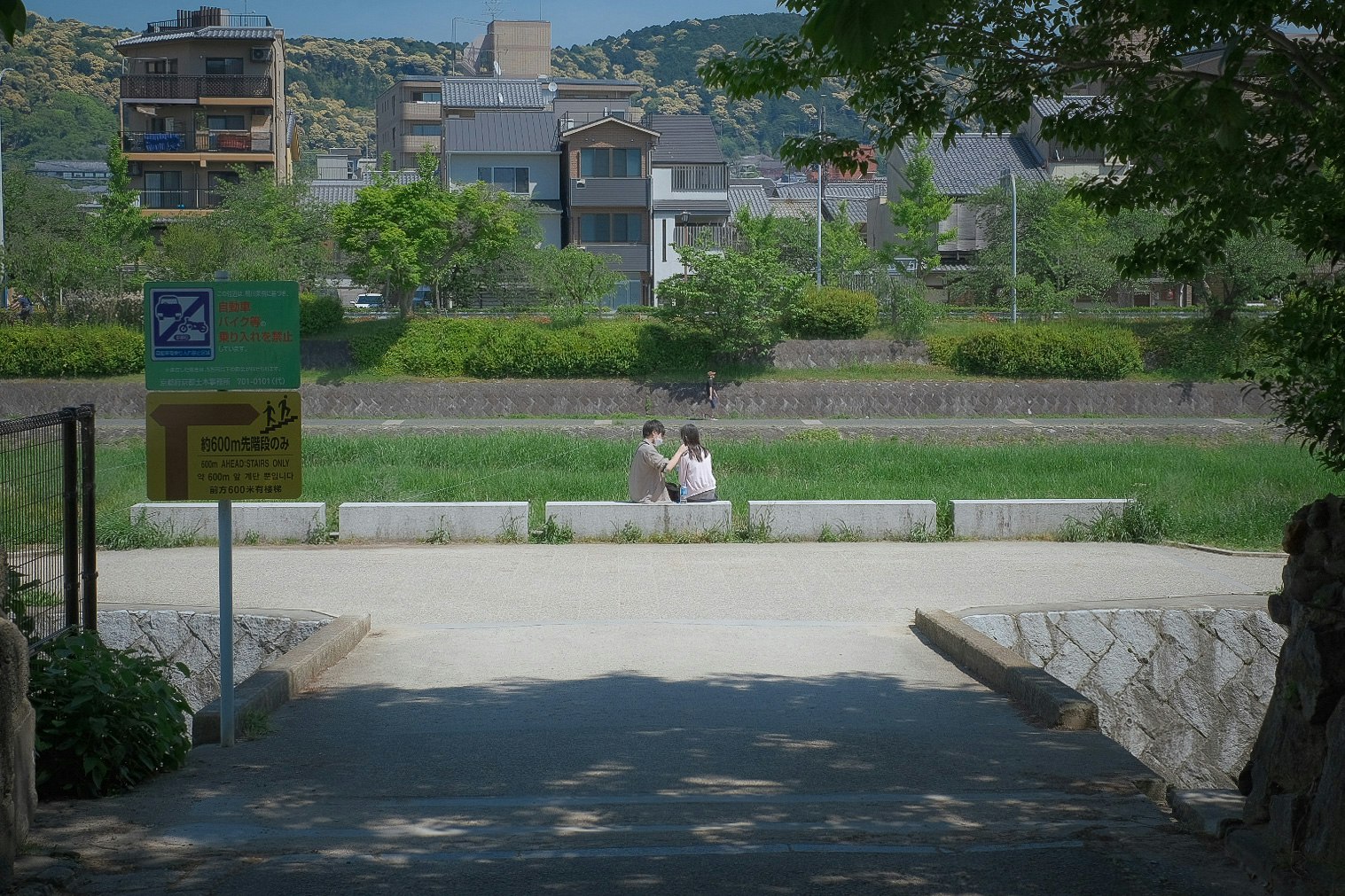 公園の小道を歩く2人の人物と緑の植栽