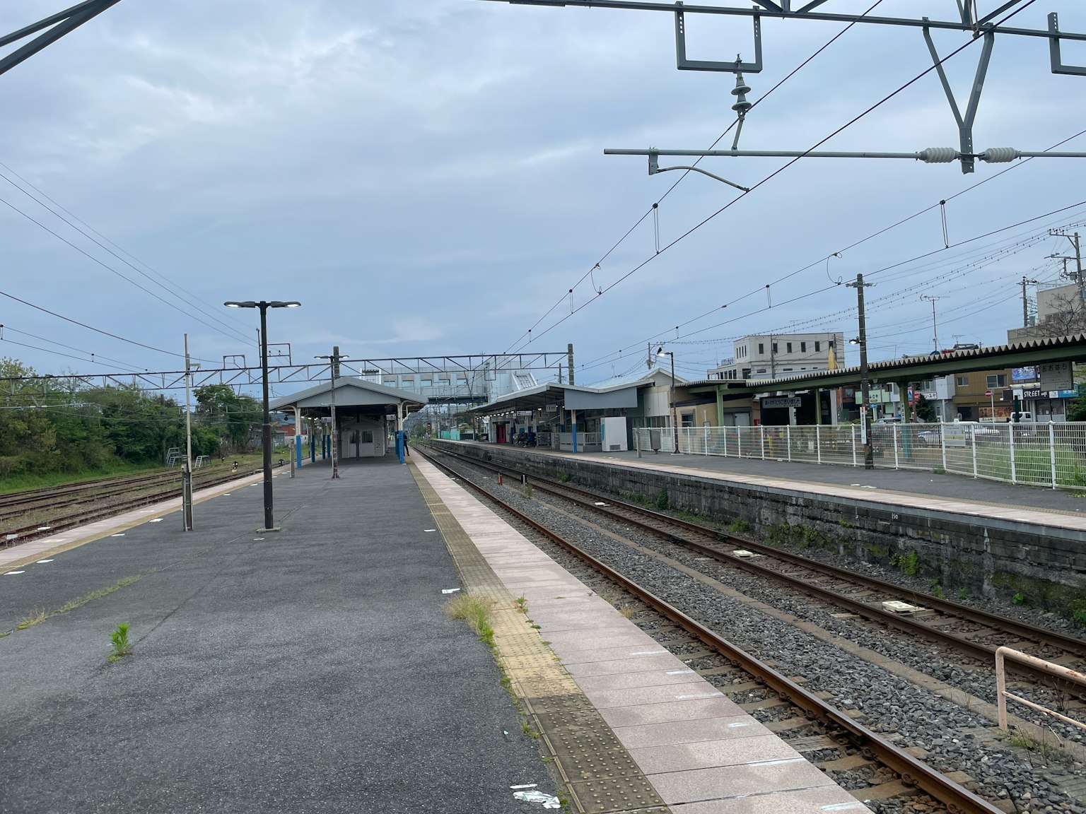 Pemandangan tenang dari platform stasiun kereta dengan rel terlihat dan langit mendung