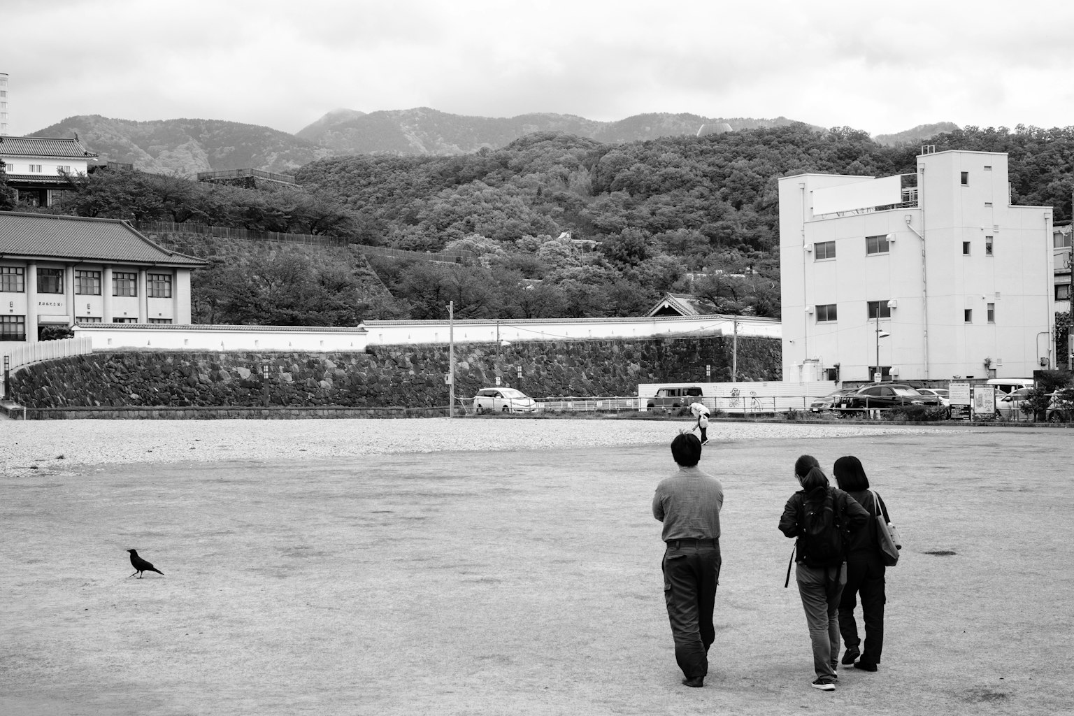 Foto in bianco e nero di persone che camminano in una piazza con montagne e edifici sullo sfondo