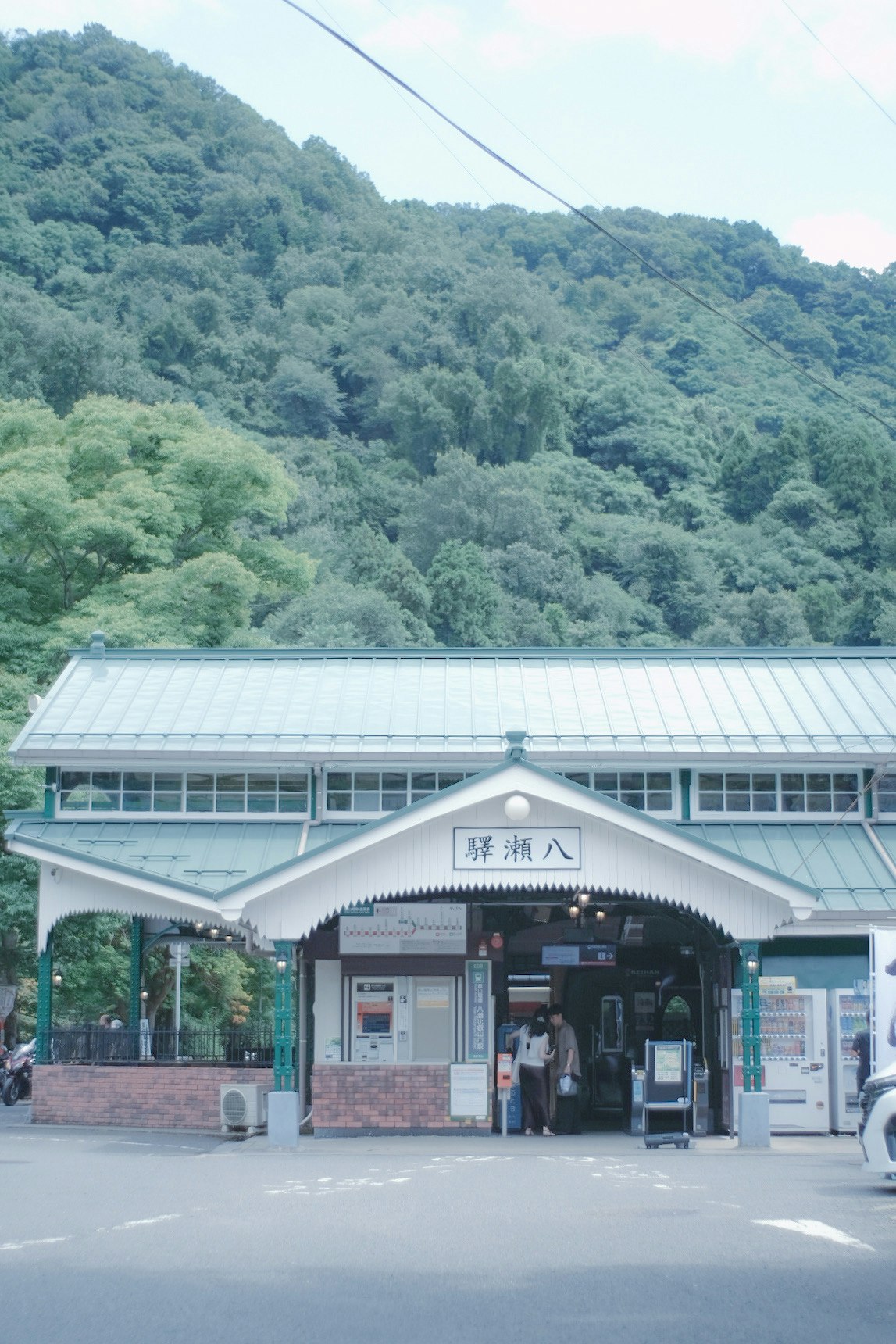 山あいの駅舎前に並ぶバス停と人