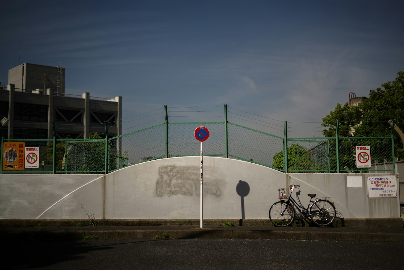 Scene with a bicycle parked in front of a green fence and white wall