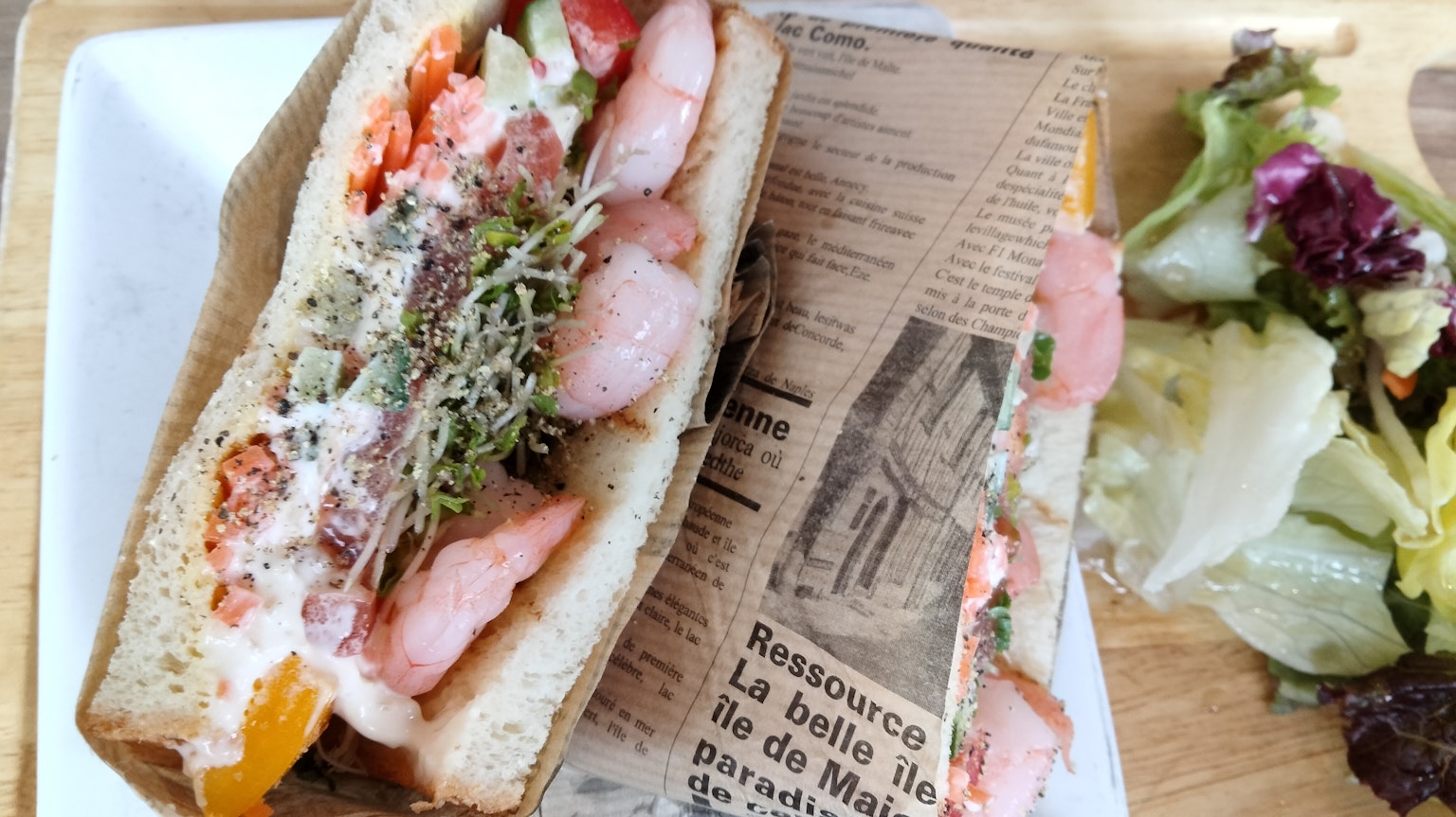Un sándwich relleno de camarones frescos y verduras servido con una ensalada
