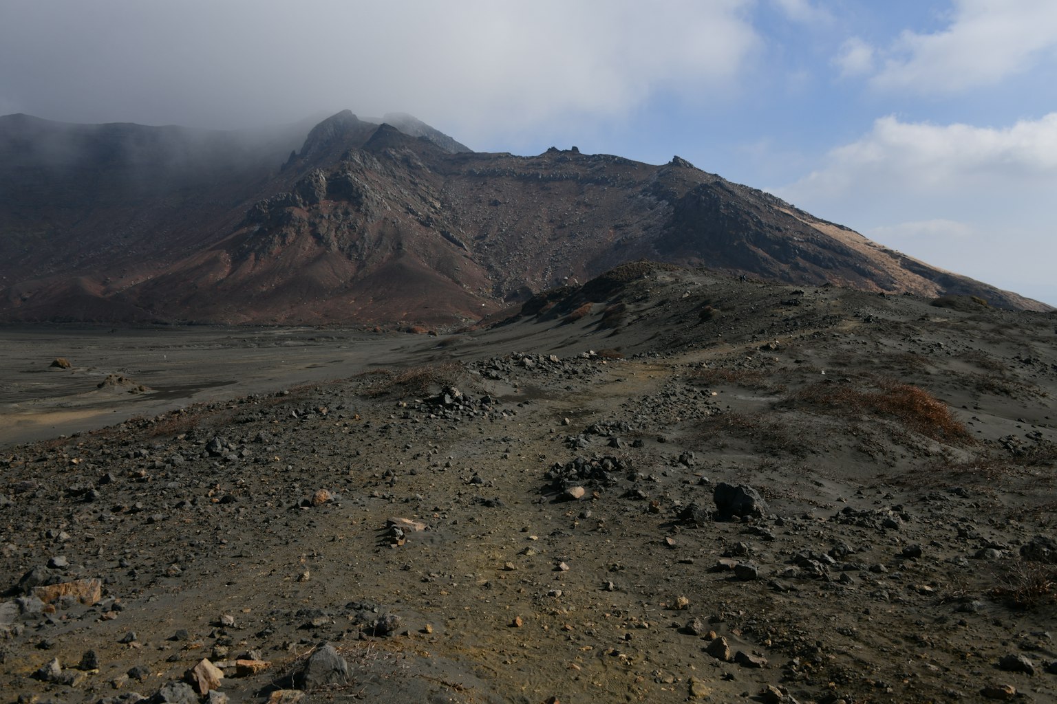 Pemandangan vulkanik yang kasar dengan gunung yang diselimuti awan