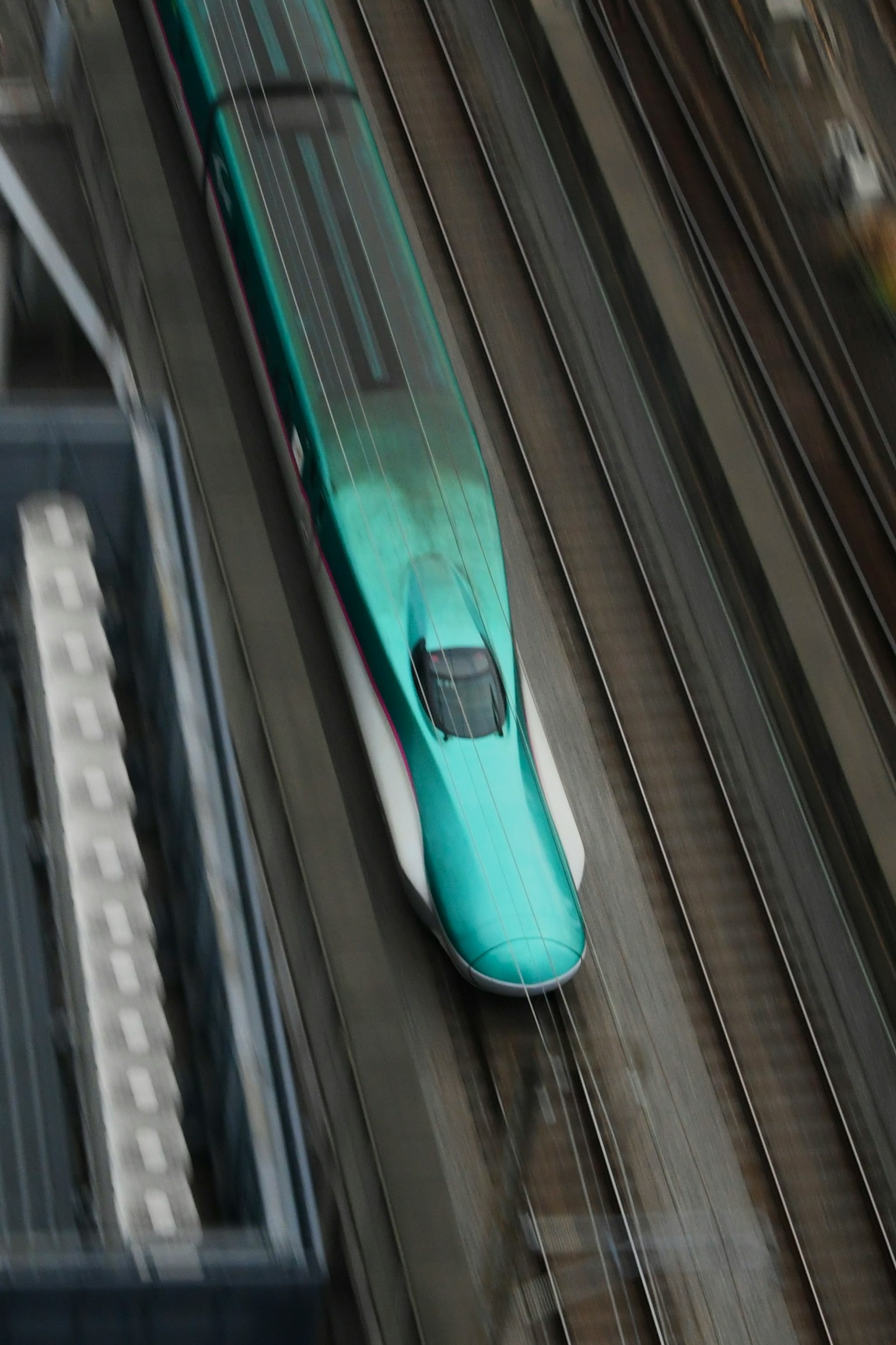 Một chiếc tàu Shinkansen màu xanh di chuyển trên đường ray từ góc nhìn trên cao
