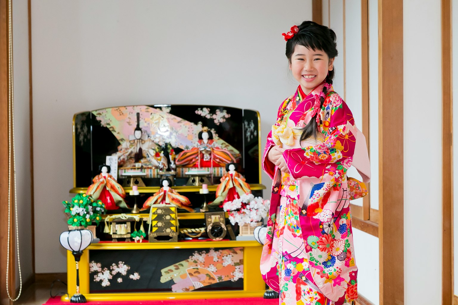 Une femme en kimono coloré se tient devant un étalage de poupées hina