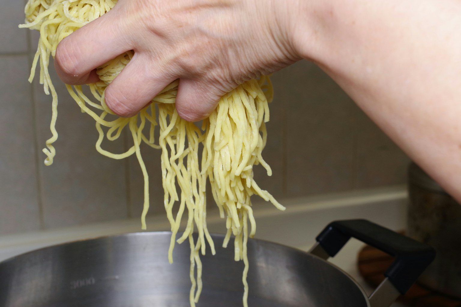 Una mano che tiene spaghetti crudi sopra una pentola pronta per la cottura