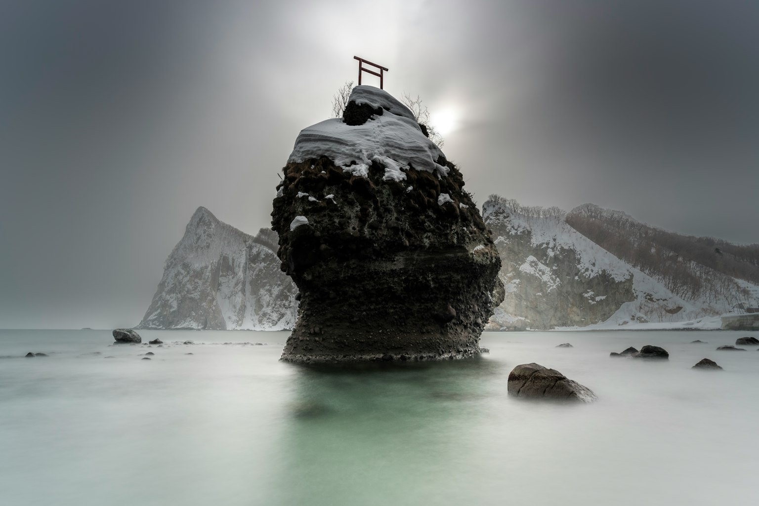 Paesaggio costiero con una roccia coperta di neve e un torii
