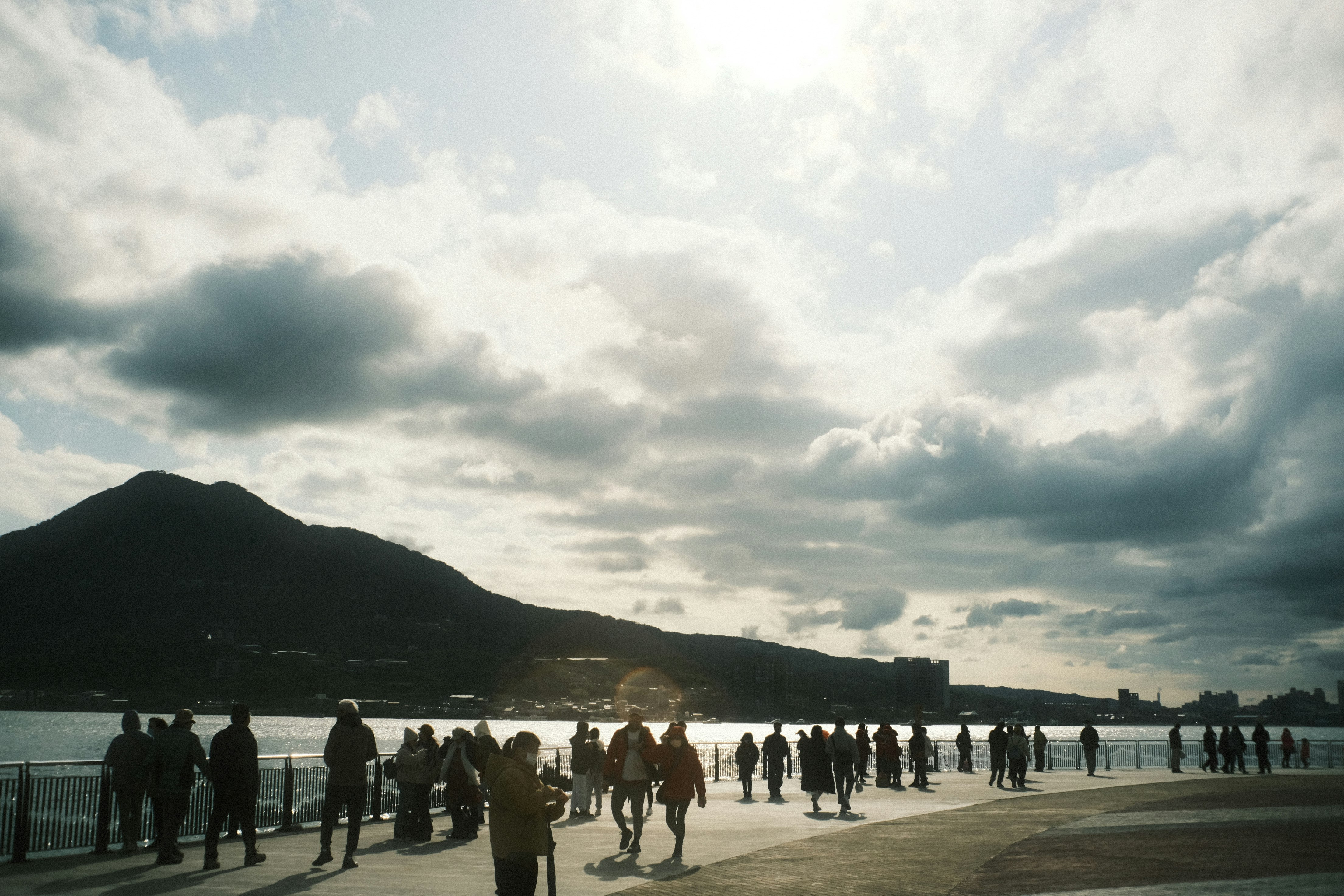 海辺の遊歩道を歩く人々と山のシルエットのある風景