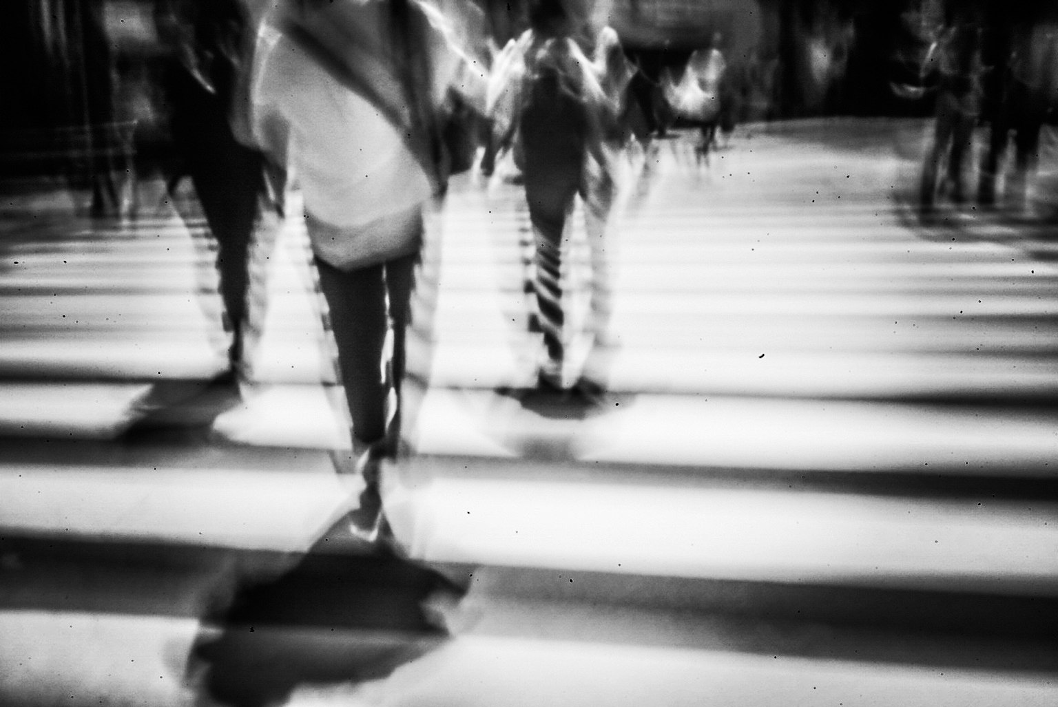 Blurred silhouettes of people walking in a crosswalk at night