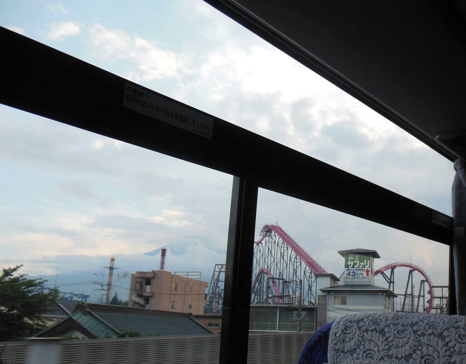 Vue d'une fenêtre de bus montrant un parc d'attractions avec des montagnes russes et une grande roue