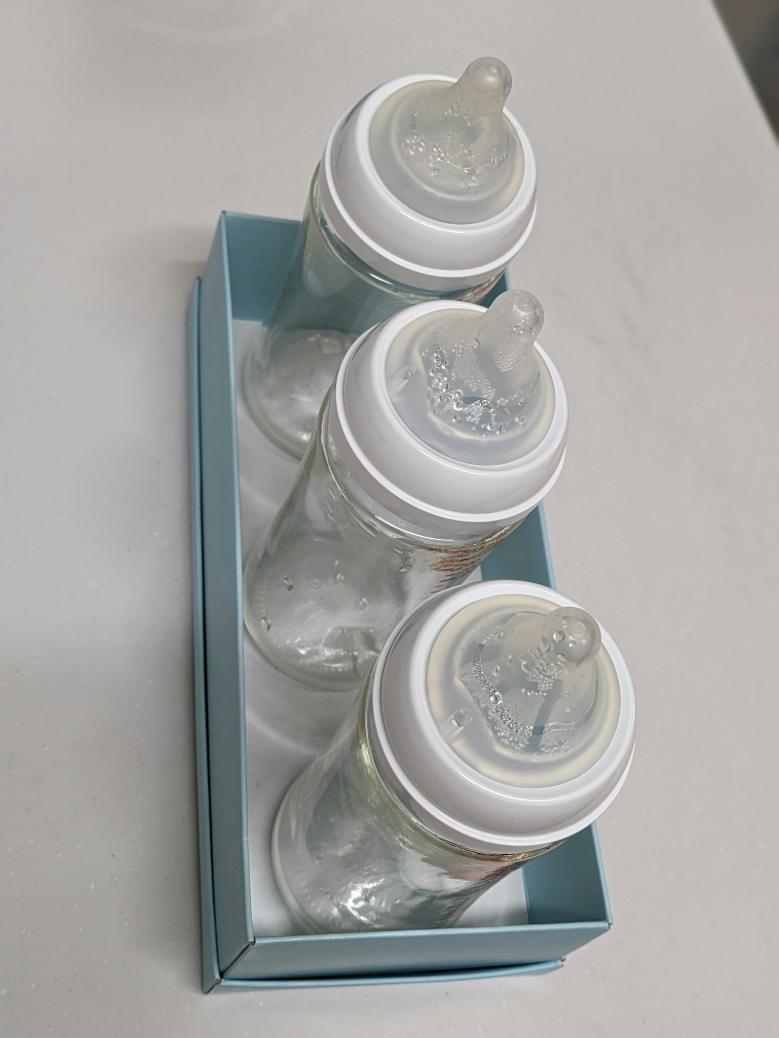 Trois biberons transparents disposés dans une boîte bleue