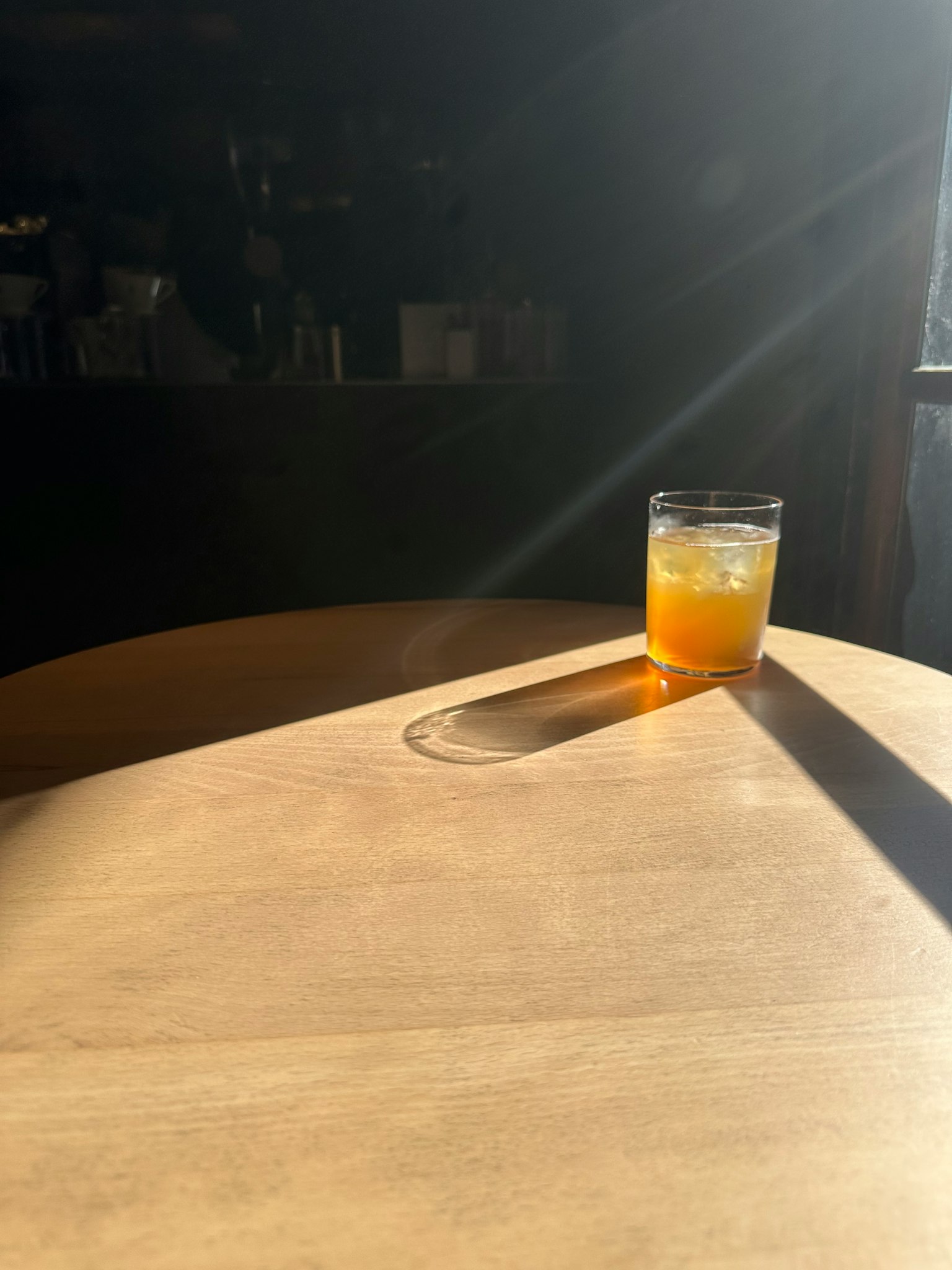 Un verre de boisson orange sur une table en bois illuminé par la lumière du soleil
