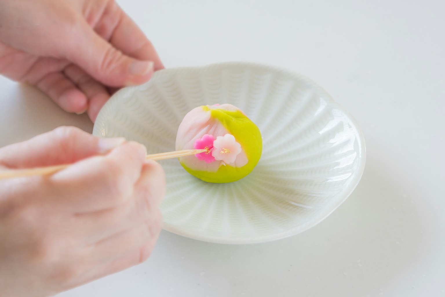 一隻手用筷子處理白盤上的多彩日本甜點