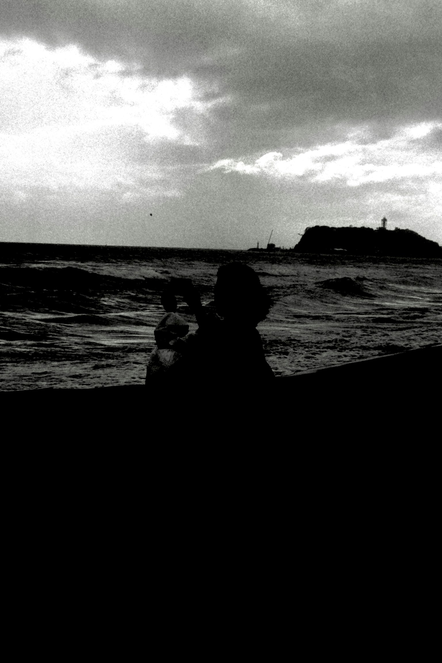 Silhouette d'une personne tenant un enfant sur la plage avec un ciel nuageux sombre